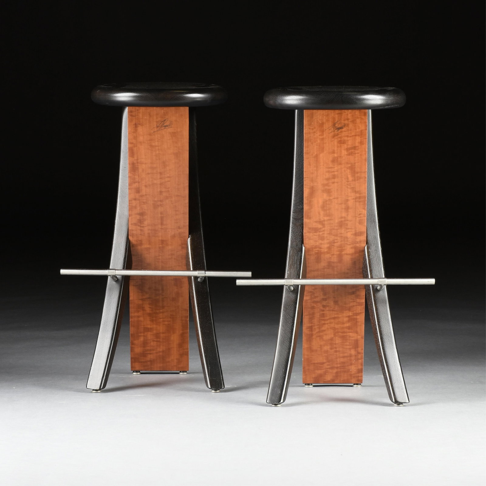 A PAIR OF ANDREW MUGGLETON "Oster Stools," ENGLISH, 21ST CENTURY, made with ebonized oak, figured: A PAIR OF ANDREW MUGGLETON "Oster Stools," ENGLISH, 21ST CENTURY, made with ebonized oak, figured makore, and stainless steel, both are signed by the designer on the makore leg, "A. Muggleton." Height