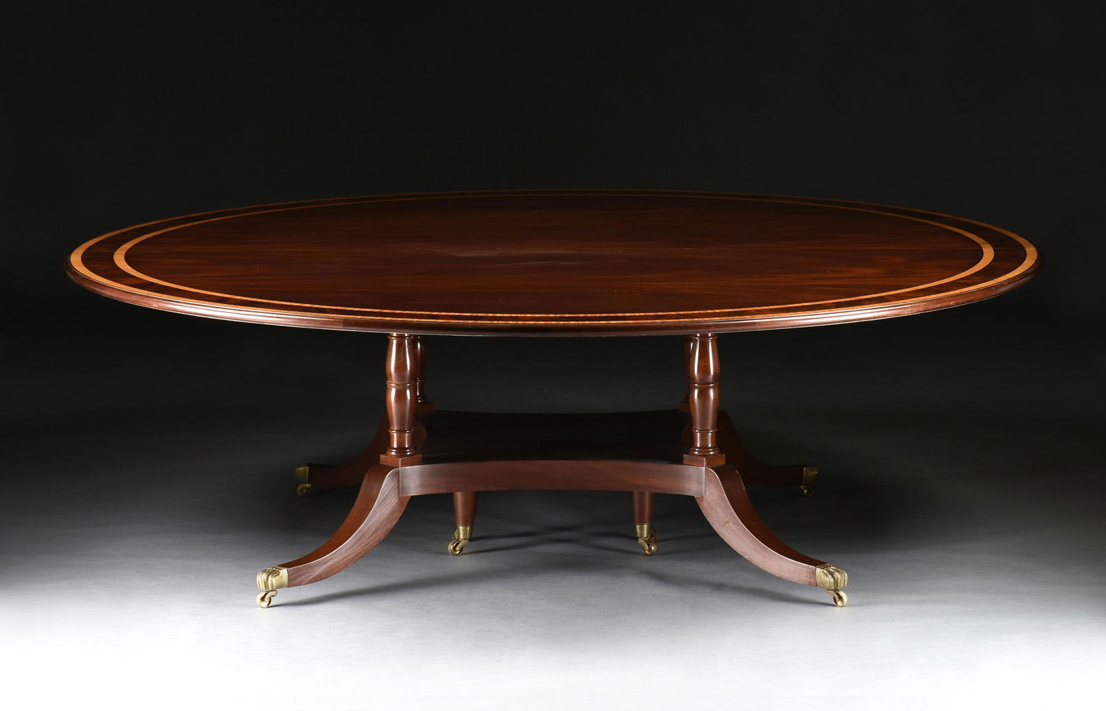 A REGENCY STYLE INLAID MAHOGANY AND SATINWOOD DINING TABLE, 21ST CENTURY,: A REGENCY STYLE INLAID MAHOGANY AND SATINWOOD DINING TABLE, 21ST CENTURY, a round inlaid mahogany and satinwood dining table with a birdcage table base, with gilt bronze paw feet on brass casters. A r