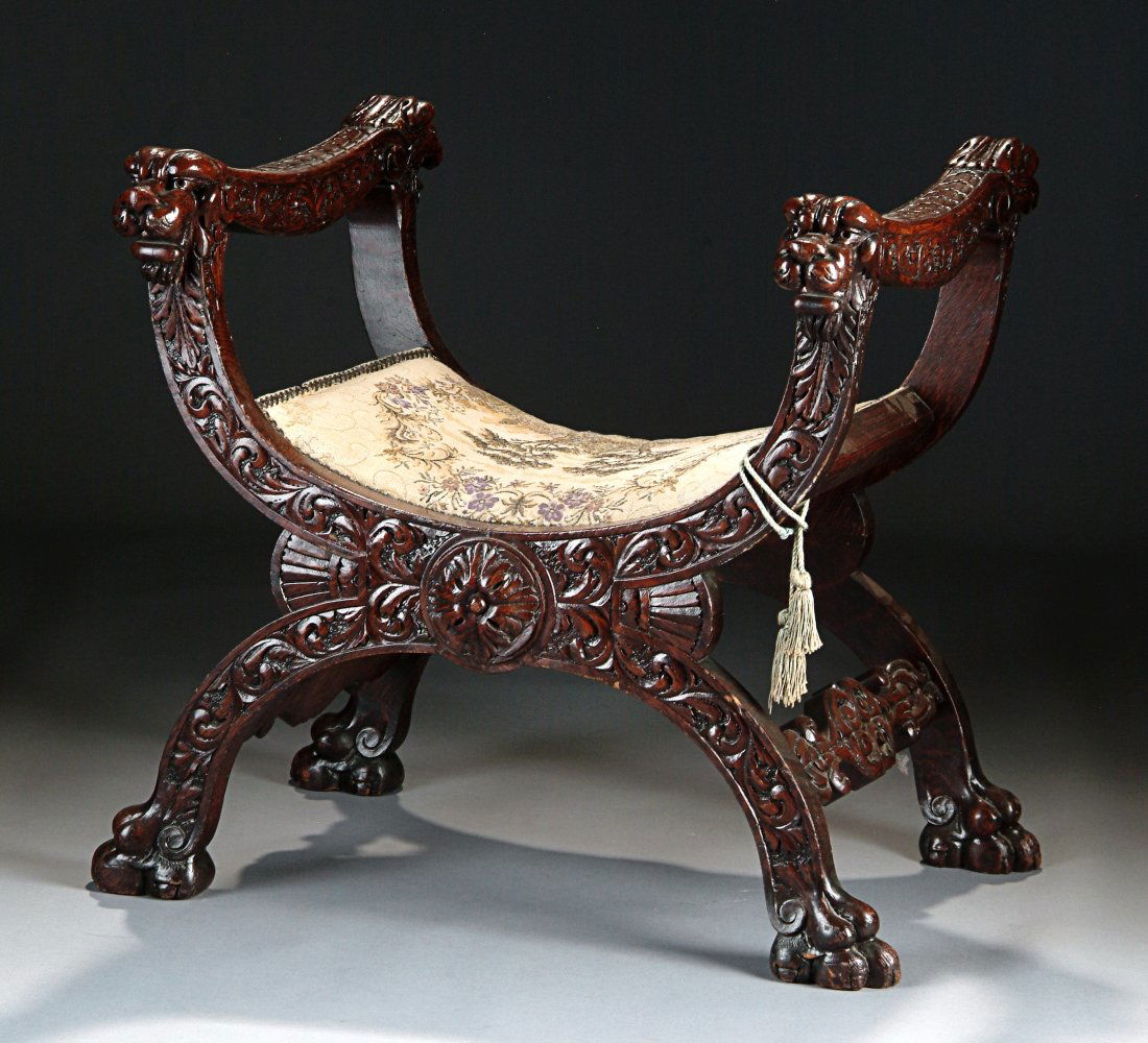 AN ITALIAN CARVED WALNUT CURULE, LATE 19TH/EARLY 20TH: AN ITALIAN CARVED WALNUT CURULE, LATE 19TH/EARLY 20TH CENTURY, of shaped "X" frame form with curved padded seat within a shallow relief sculptured frame of scrolling foliage beneath lion's head termin
