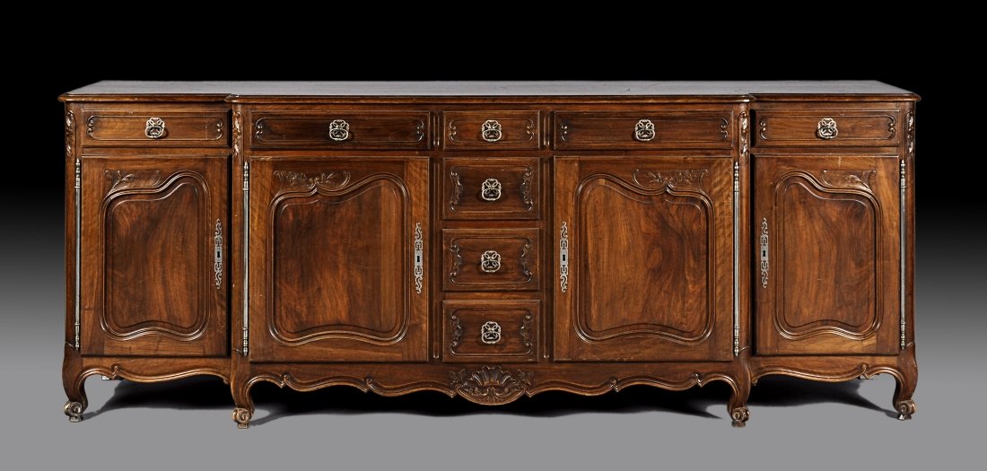 A FRENCH PROVINCIAL STYLE CARVED WALNUT BUFFET GRAND, E: A FRENCH PROVINCIAL STYLE CARVED WALNUT BUFFET GRAND, EARLY 20TH CENTURY, the breakfront rectangular top above four paneled frieze drawers centering four stacked and graduated short drawers flanked by