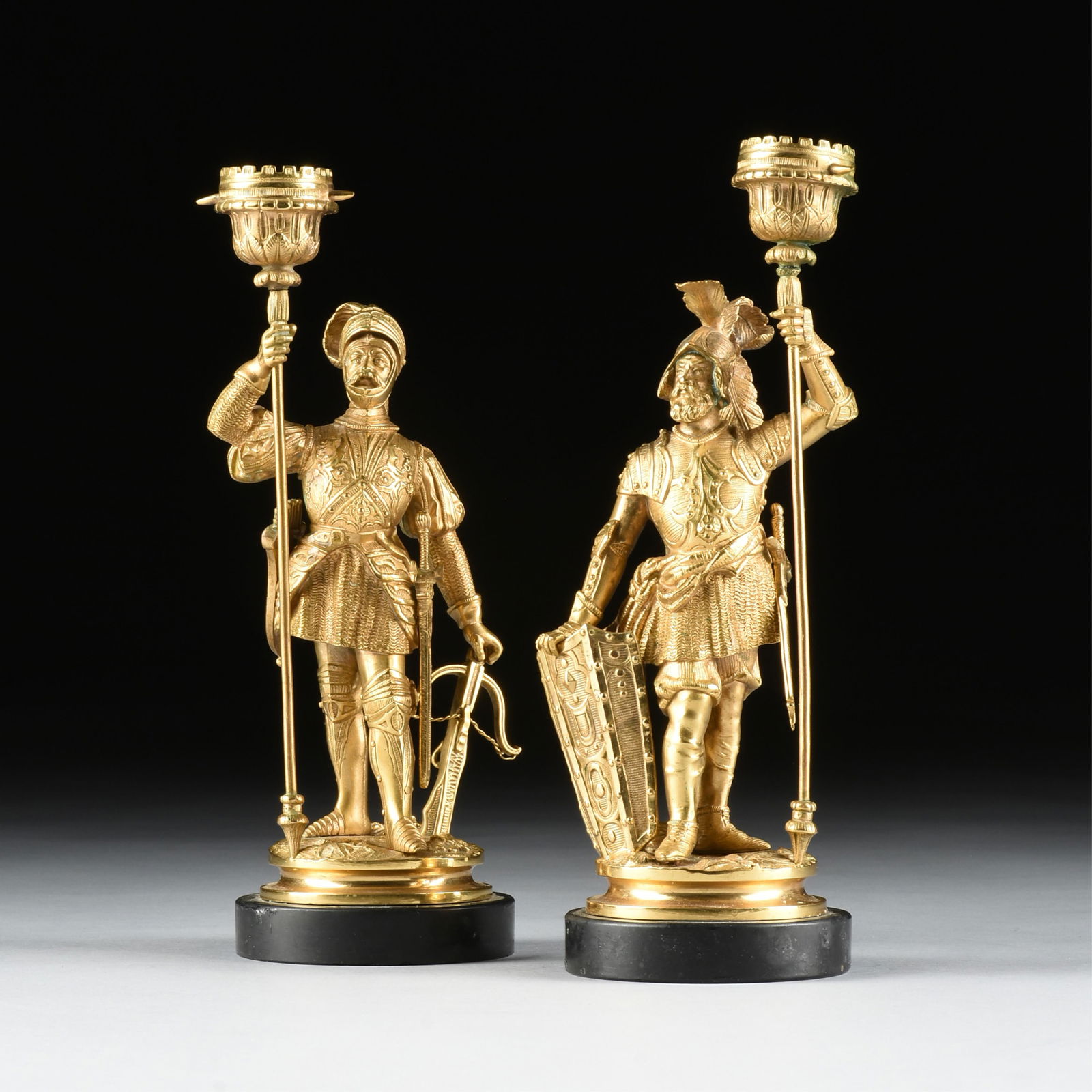 A PAIR OF MEDIEVAL KNIGHT CANDLESTICKS, 19TH/20TH CENTURY,: A PAIR OF MEDIEVAL KNIGHT CANDLESTICKS, 19TH/20TH CENTURY,gilt bronze candlesticks in the form of European knights, each mounted on a black stone base.Each: 10 1/2 x 3 3/4 x 3 3/4 in. (26.7 x 9.5 x 9.