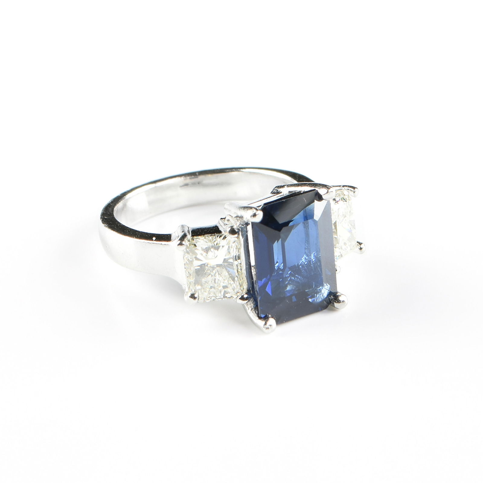 A PLATINUM, BURMESE SAPPHIRE, AND DIAMOND RING, 20TH/21ST CENTURY,: A PLATINUM, BURMESE SAPPHIRE, AND DIAMOND RING, 20TH/21ST CENTURY,a platinum ring with an emerald cut deep blue Burmese sapphire, H approximately 4.5 cts., flanked by two radiant cut diamonds, L one S