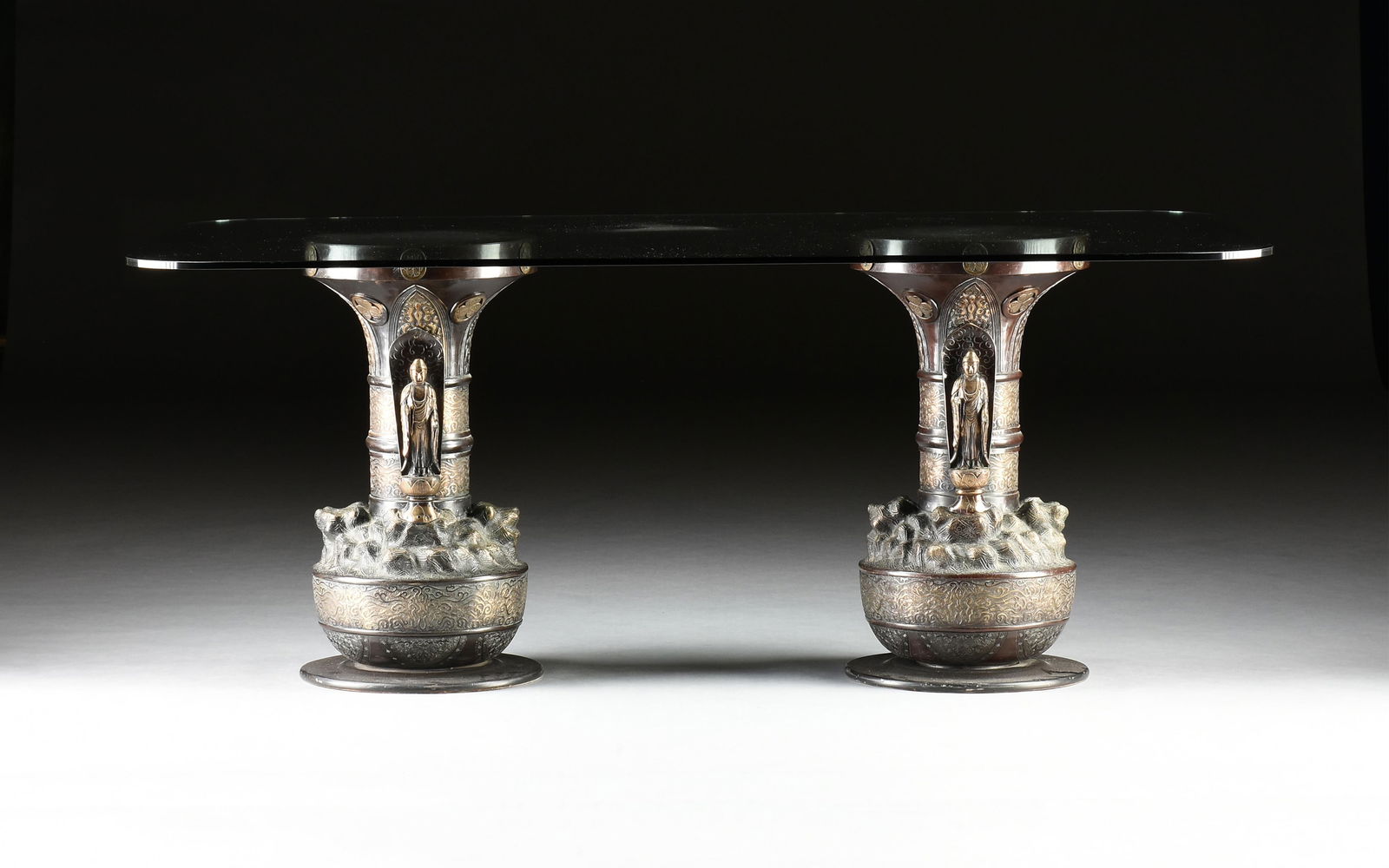 A TWO PEDESTAL GLASS TOPPED DINING TABLE,: A TWO PEDESTAL GLASS TOPPED DINING TABLE,the modern glass top of rectangular form with rounded edges, raised on a pair of older matching Japanese patinated and gilt metal pedestals, of vasiform shape,