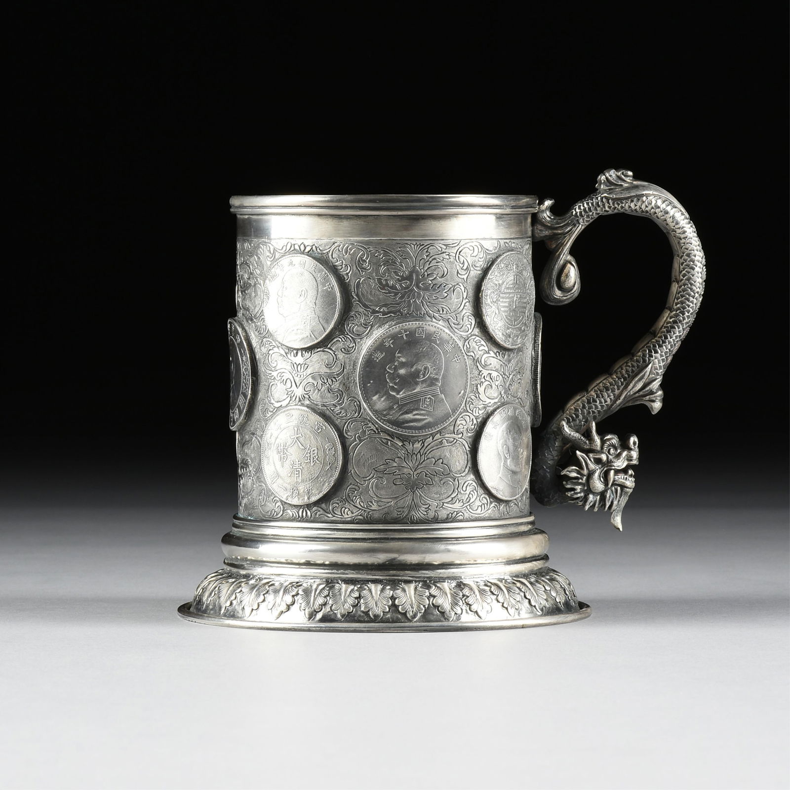 A LEECHING COIN SILVER TANKARD, CHINESE EXPORT, EARLY 20TH CENTURY,: A LEECHING COIN SILVER TANKARD, CHINESE EXPORT, EARLY 20TH CENTURY,a coin silver tankard decorated with coins, foliate engraving, and a sculptural dragon handle, marked on base, "LEECHING 90," and wit