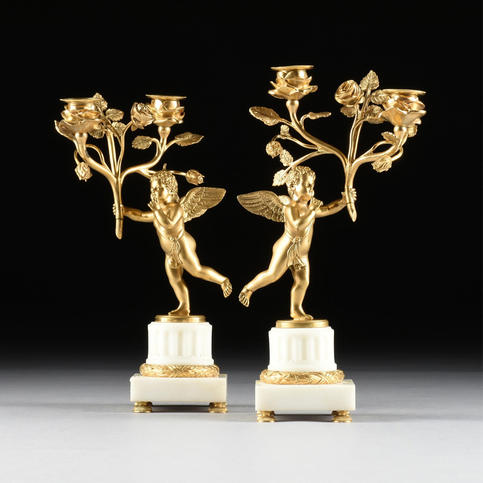 A PAIR OF NEOCLASSICAL STYLE TWO-LIGHT PUTTI CANDELABRA, FRENCH, 20TH CENTURY,: A PAIR OF NEOCLASSICAL STYLE TWO-LIGHT PUTTI CANDELABRA, FRENCH, 20TH CENTURY,two painted metal and marble candelabra.Each: 12 x 6 1/2 x 3 1/2 in. (30.5 x 16.5 x 8.9 cm.) Provenance: Collection of the