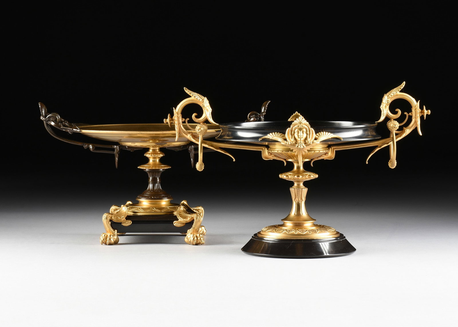 TWO NEOCLASSICAL STYLE BRONZE ORMOLU TAZZAS, 20TH CENTURY,: TWO NEOCLASSICAL STYLE BRONZE ORMOLU TAZZAS, 20TH CENTURY, two gilt bronze tazzas, each mounted on a marble base, one with a black bowl and a gilt central medallion of a woman's head in profile, and t