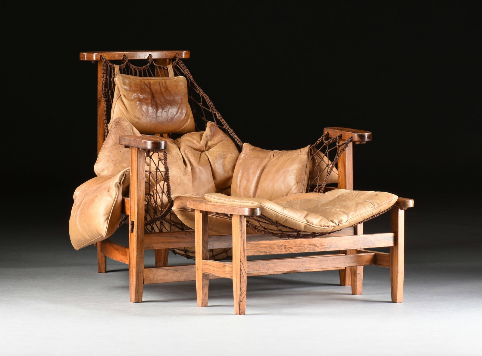 JEAN GILLON (Romanian 1919-2007) A JANGADA CHAIR AND OTTOMAN, CIRCA 1970,: JEAN GILLON (Romanian 1919-2007) A JANGADA CHAIR AND OTTOMAN, CIRCA 1970, mid-century modern rosewood and nylon cord with leather upholstery. Chair: 32 x 34 1/2 x 40 in. (81.3 x 87.6 x 101.6 cm.), Ott