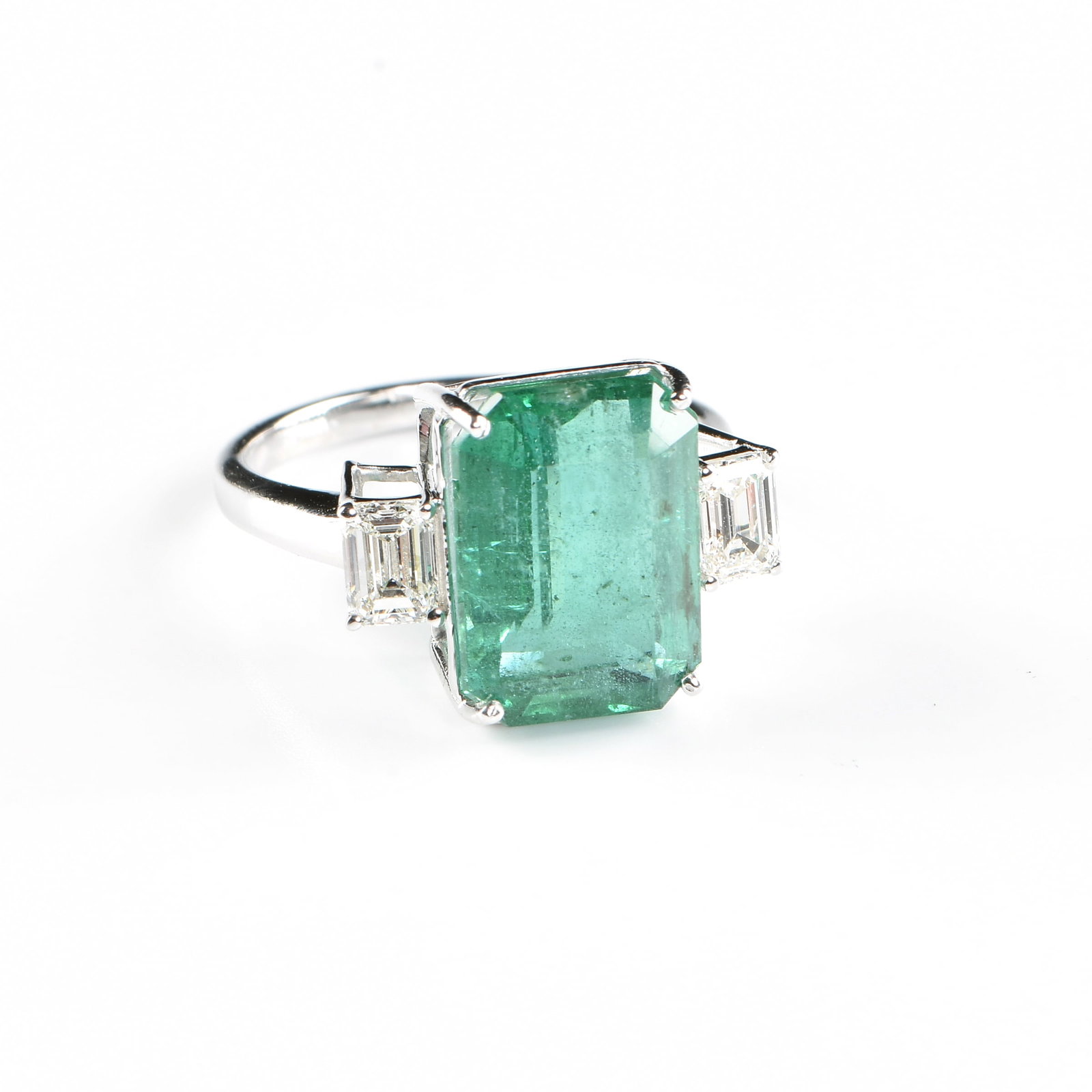 AN 18K GOLD, ZAMBIAN EMERALD, AND DIAMOND RING,: AN 18K GOLD, ZAMBIAN EMERALD, AND DIAMOND RING, 18k white gold ring set with a 5.44 carat octagonal step-cut Zambian emerald with a rich, medium-deep green color, flanked by a matched pair of emerald 