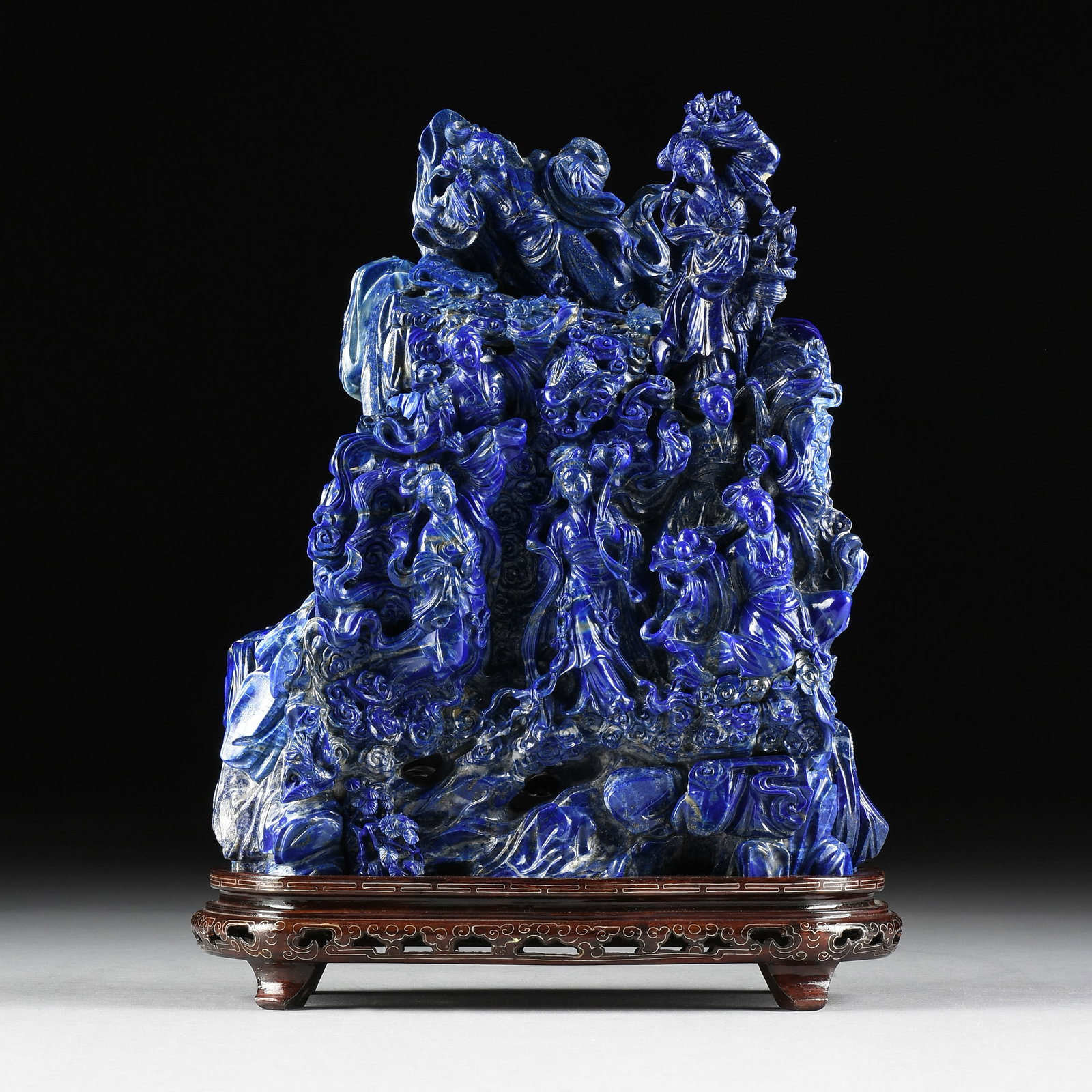 A CARVED LAPIS SCULPTURE, CHINESE, 20TH CENTURY,: A CARVED LAPIS SCULPTURE, CHINESE, 20TH CENTURY, carved and assembled lapis stones portraying six women, birds, and flowers, and with a wooden stand. 13 x 11 1/4 x 5 in. (33 x 28.6 x 12.7 cm.) Provena