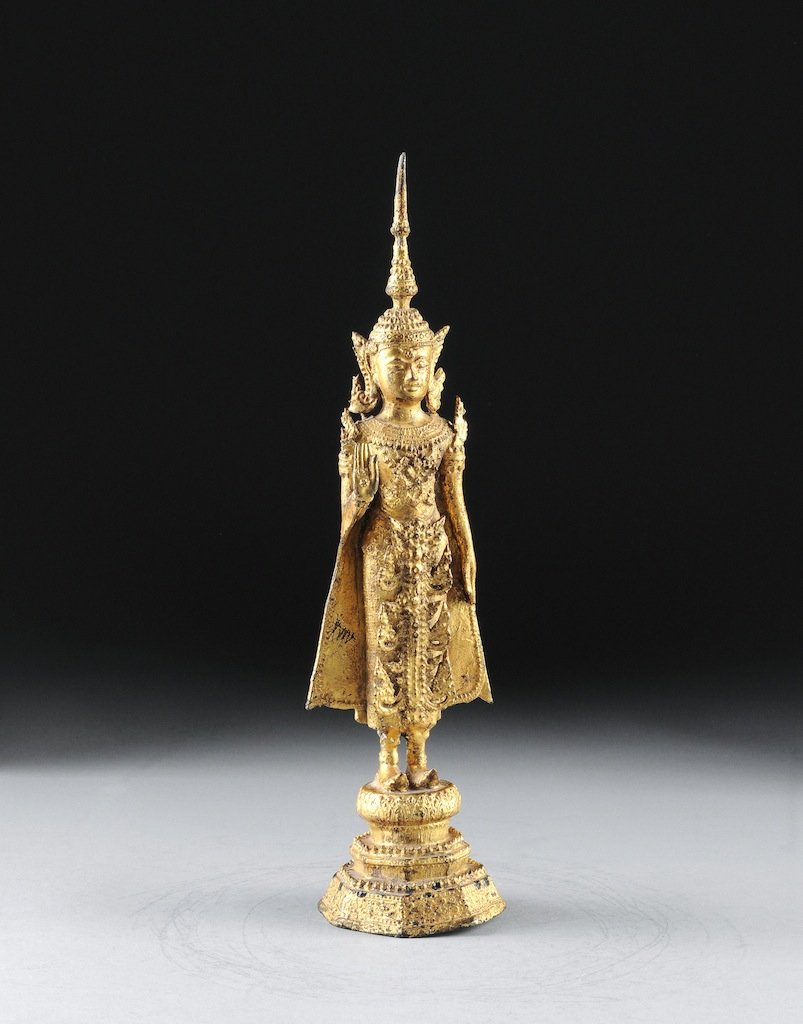 AN ANTIQUE THAI PARCEL GILT BRONZE FIGURE OF SHAKYAMUNI: AN ANTIQUE THAI PARCEL GILT BRONZE FIGURE OF SHAKYAMUNI, 19TH CENTURY, cast in standing position having a serene expression, with hands in abhaya and dada-mudra,wearing an elaborate pointed headdress 