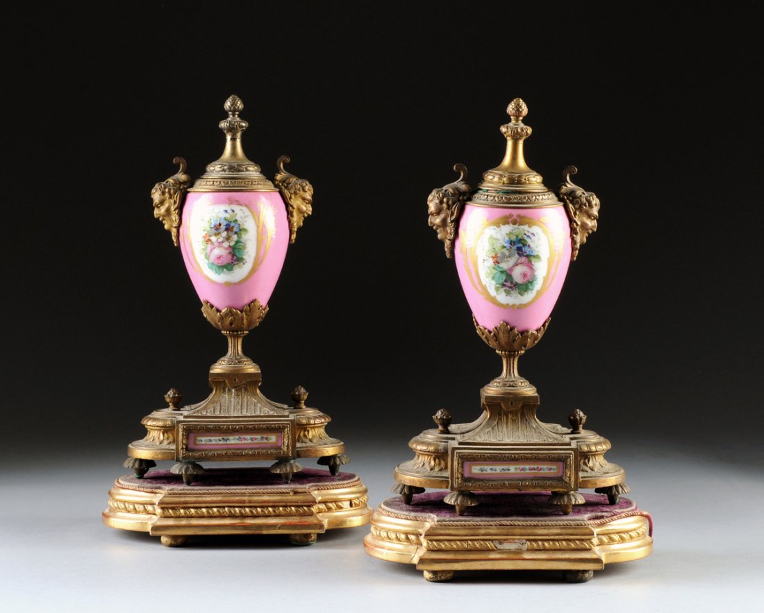 A PAIR OF SÉVRES STYLE VASIFORM GARNITURE URNS, 19TH: A PAIR OF SEVRES STYLE VASIFORM GARNITURE URNS, 19TH CENTURY, the porcelain urns with pink ground centering a hand painted floral cartouche with gilt paint decoration, the shoulders flanked by gilt br