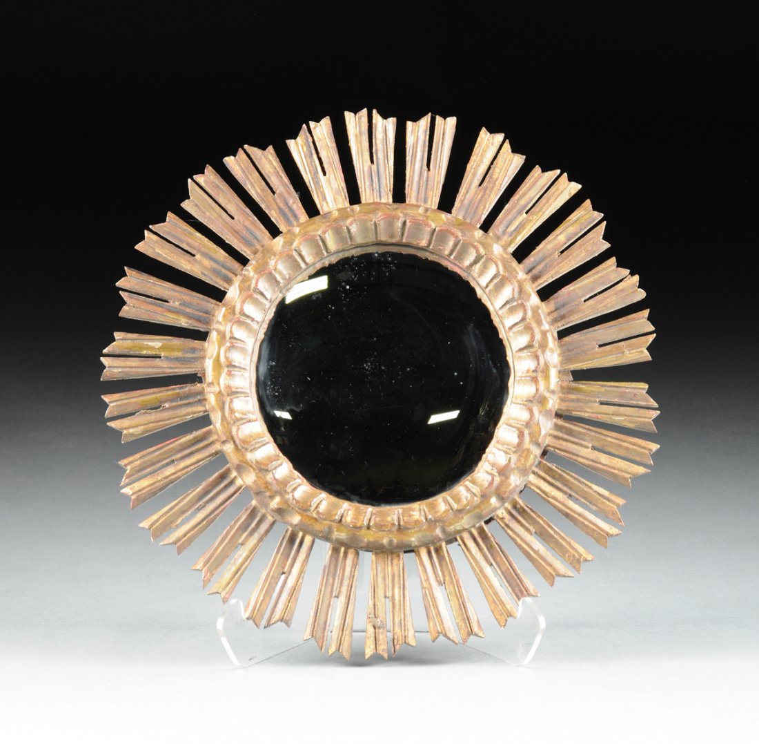 AN ITALIAN PARCEL GILT AND CARVED WOOD SUNBURST CONVEX: AN ITALIAN PARCEL GILT AND CARVED WOOD SUNBURST CONVEX MIRROR, MID 20TH CENTURY. the circular convex mirror enclosed by a conforming scalloped frame issuing stylized sun rays. Diameter: 19 1/2"