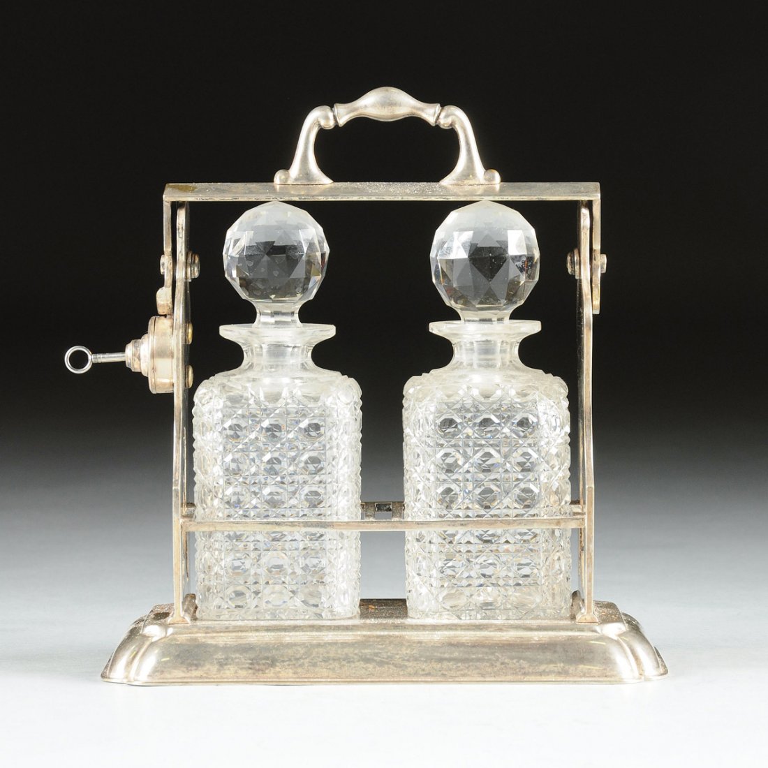 A VICTORIAN LEAD CRYSTAL AND SILVER PLATED TWO BOTTLE: A VICTORIAN LEAD CRYSTAL AND SILVER PLATED TWO BOTTLE LIQUOR TANTALUS, JOHN GRINSELL & SONS, BIRMINGHAM, ENGLAND, LATE 19TH CENTURY, the silver plated frame with baluster form uprights with trefoil cu