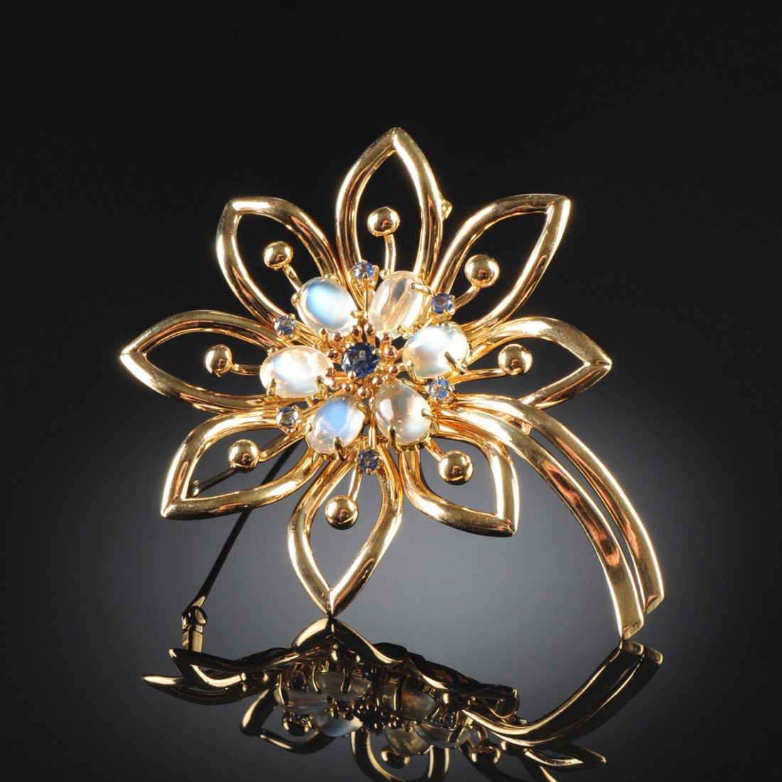 A 14K YELLOW GOLD, SAPPHIRE, AND DIAMOND LADY"S FLOWER: A 14K YELLOW GOLD, SAPPHIRE, AND DIAMOND LADY"S FLOWER BROOCH, measuring 2 1/2” x 3 1/8” and highlighted with six oval moonstones and seven blue sapphires. Excellent condition.