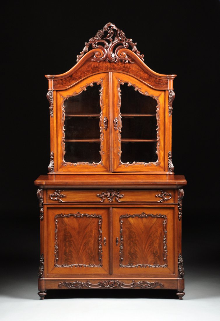 A VICTORIAN CARVED MAHOGANY CABINET VITRINE, CIRCA: A VICTORIAN CARVED MAHOGANY CABINET VITRINE, CIRCA 1880, in the Rococo Revival style and having a scrolling arched cornice surmounted by a reticulated blossoming "C" scroll pendant above a flame mahog