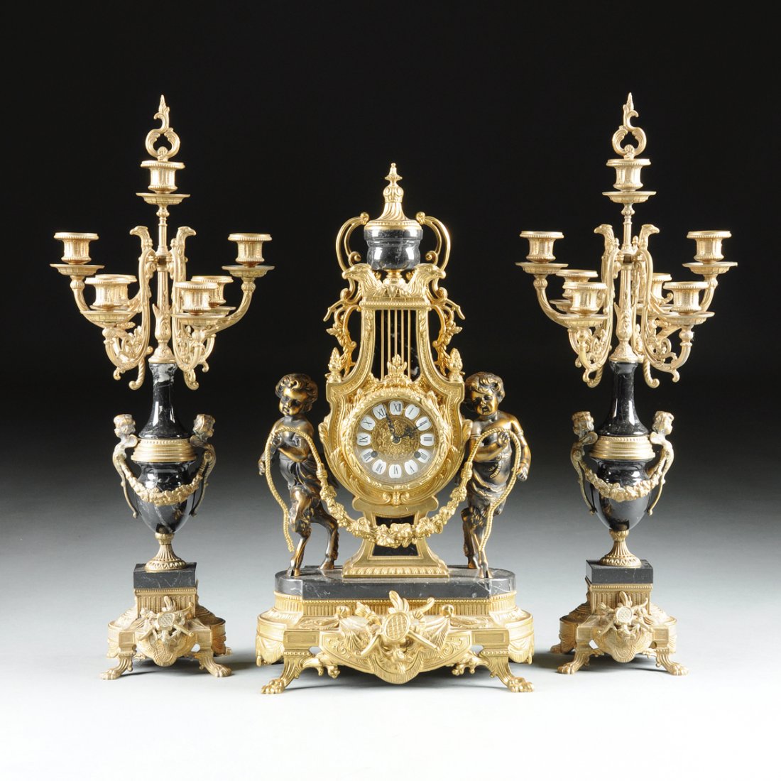 A THREE PIECE LOUIS XVI STYLE GILT BRONZE AND BLACK: A THREE PIECE LOUIS XVI STYLE GILT BRONZE AND BLACK MARBLE LYRE FORM MANTLE CLOCK AND CANDELABRA GARNITURE, CLOCK MECHANISM BY FRANZ HERMTE, LATE 20TH CENTURY, the circular dial with black Roman hour 