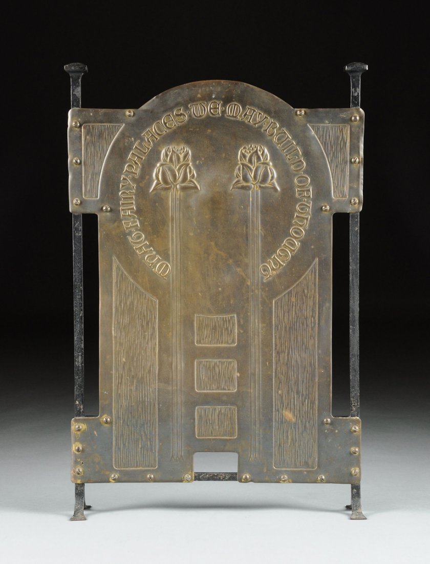 AN ENGLISH ARTS & CRAFTS BRASS AND WROUGHT IRON FIRE: AN ENGLISH ARTS & CRAFTS BRASS AND WROUGHT IRON FIRE SCREEN ATTRIBUTED TO CHARLES FRANCIS ANNESLEY VOYSEY, CIRCA 1900, with repoussé stylized tulip decoration and domed reflector wrapped with motto "