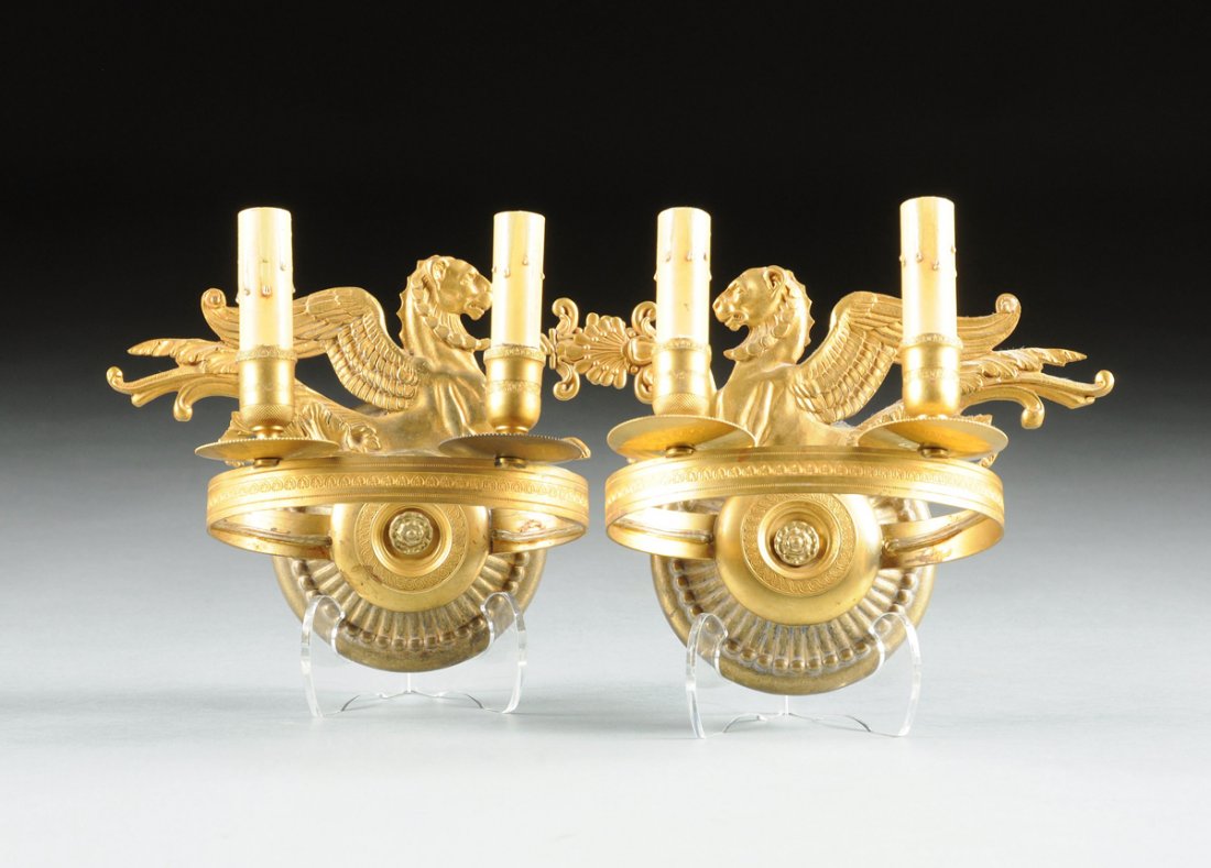 A PAIR OF DIRECTOIRE STYLE GILT BRONZE TWO-LIGHT WALL: A PAIR OF DIRECTOIRE STYLE GILT BRONZE TWO-LIGHT WALL APPLIQUES, 20TH CENTURY, each cast with a back plate modeled as a profile winged lion holding aloft a stylized anthemion above a circular reeded d