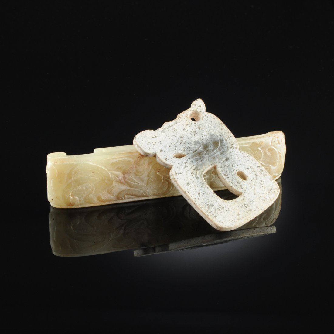 TWO CHINESE ARCHAISTIC STYLE CARVED JADE OBJECTS,: TWO CHINESE ARCHAISTIC STYLE CARVED JADE OBJECTS, comprising an Eastern Zhou Dynasty Style flat reticulated stylized dragon pendant with scrolling tail and line details, in a black mottled beige jade,