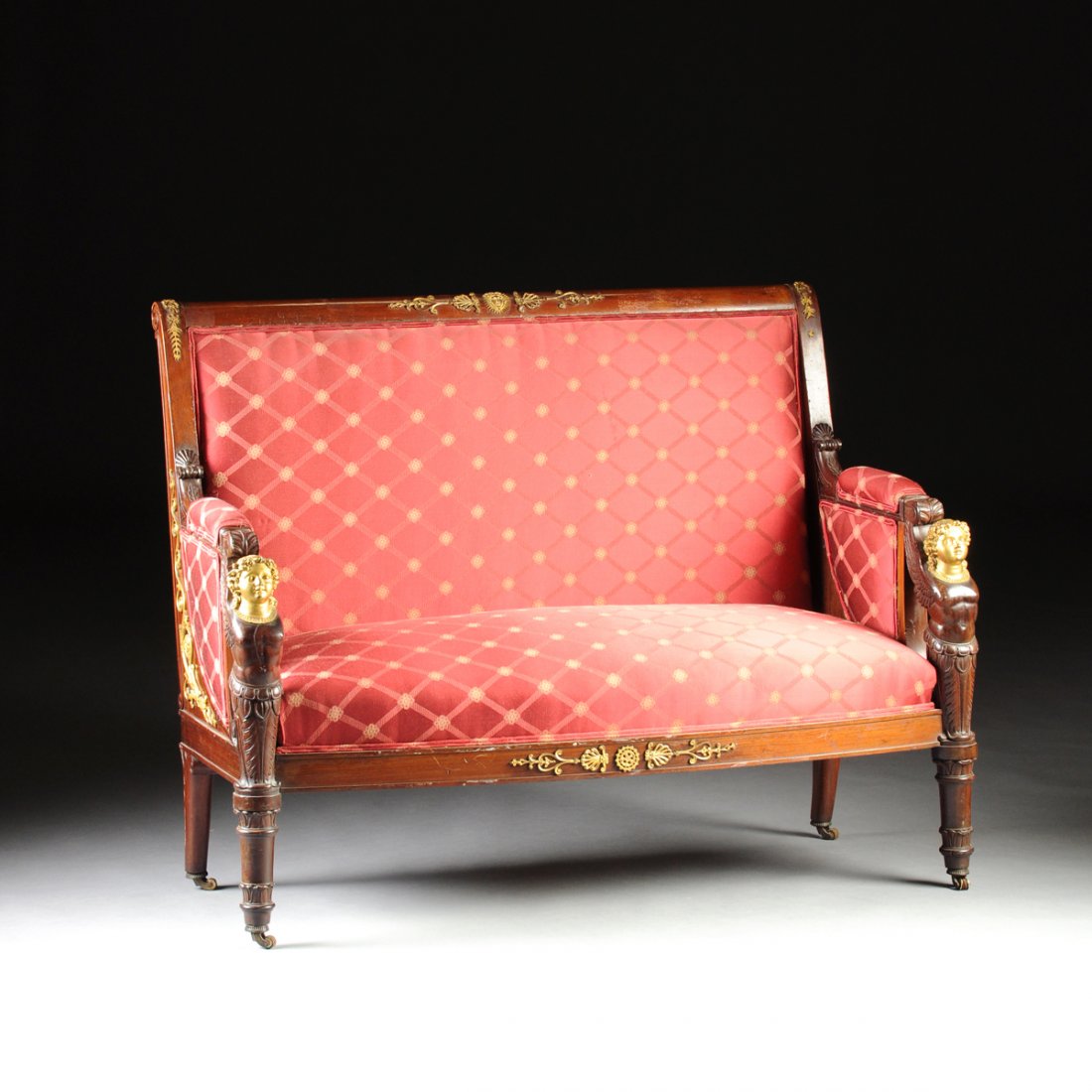 AN EMPIRE STYLE GILT BRONZE MOUNTED AND RED SILK: AN EMPIRE STYLE GILT BRONZE MOUNTED AND RED SILK UPHOLSTERED MAHOGANY SETTEE, FOURTH QUARTER 19TH CENTURY, with a scrolled crestrail centering an Apollo mask mount flanked by lozenge form pendants abo