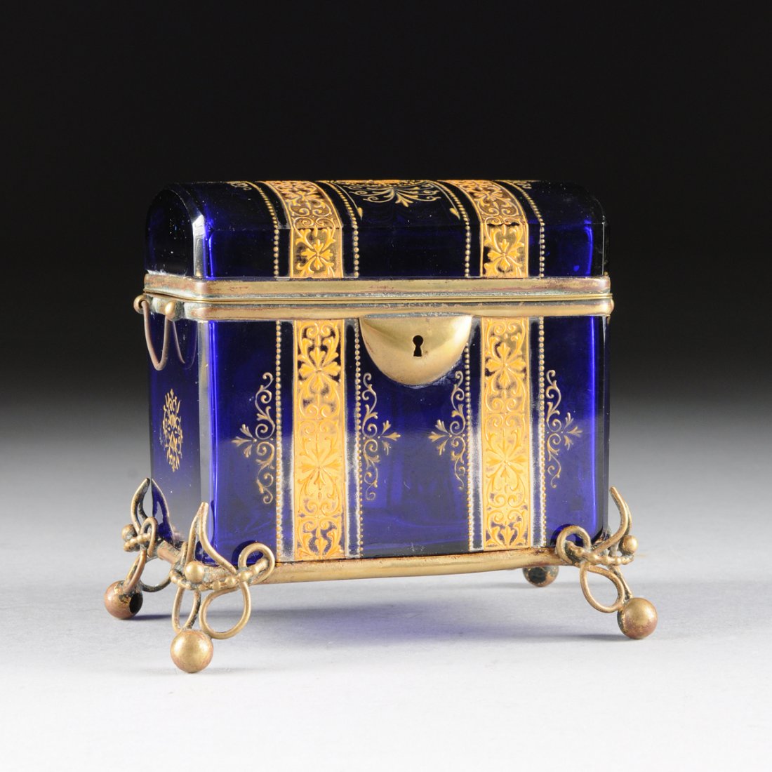 A BOHEMIAN COBALT BLUE GLASS GILT METAL MOUNTED CASKET,: A BOHEMIAN COBALT BLUE GLASS GILT METAL MOUNTED CASKET, CIRCA 1880, rectangular top with domed lid decorated with banded orange enamel and raised gilt arabesque decoration flanked by bands of beading 