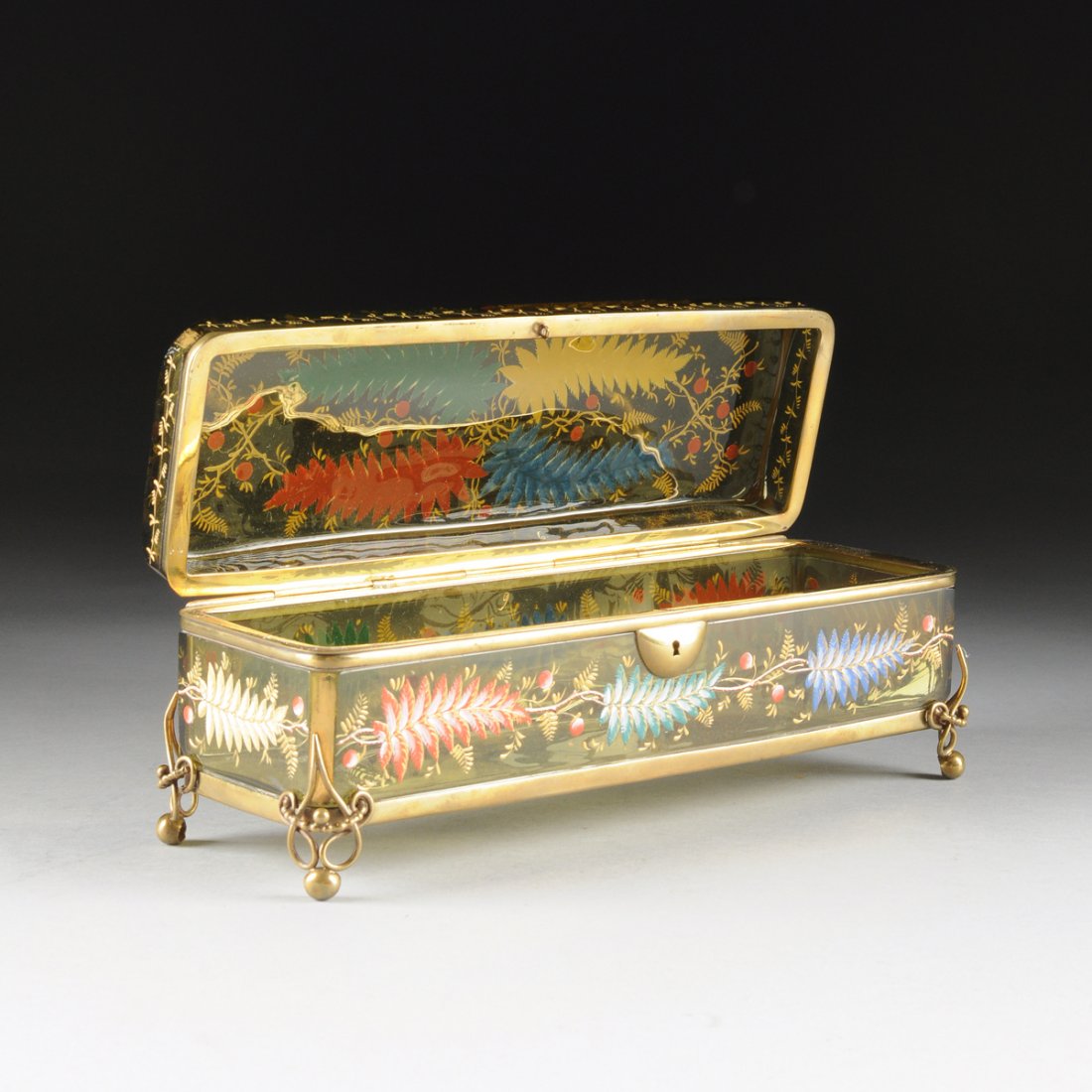 A BOHEMIAN GILT METAL MOUNTED AMBER GLASS GLOVE BOX,: A BOHEMIAN GILT METAL MOUNTED AMBER GLASS GLOVE BOX, CIRCA 1880, rectangular with enamel pine branch and berry decoration with gilt highlights, gilt banding at edges, fitted with gilt metal frame and 