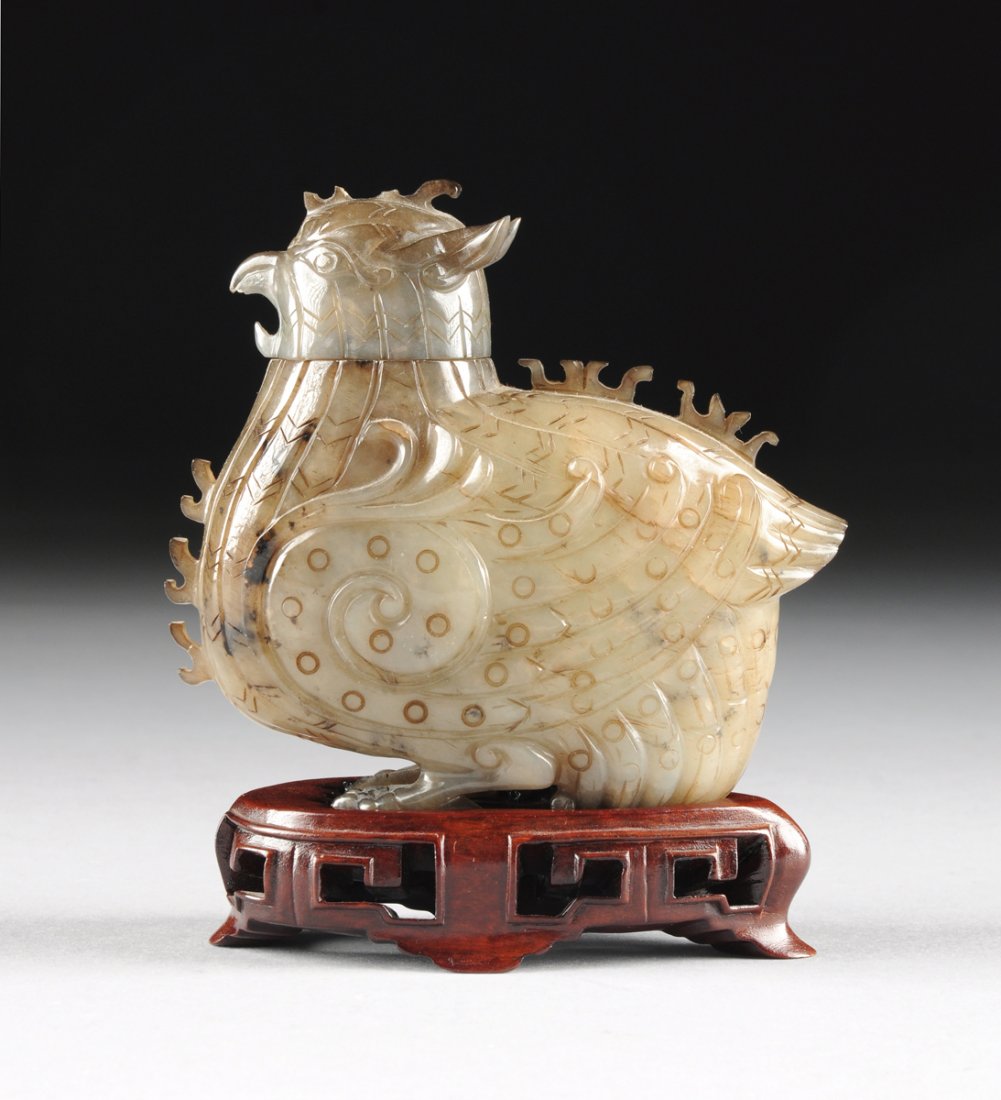 A CHINESE ARCHAISTIC STYLE CARVED JADE BIRD FORM JAR,: A CHINESE ARCHAISTIC STYLE CARVED JADE BIRD FORM JAR, MODERN, of smokey celadon jade with russet brown to blackish inclusions and depicting a stylized scrolling winged bird, with back and breast feath