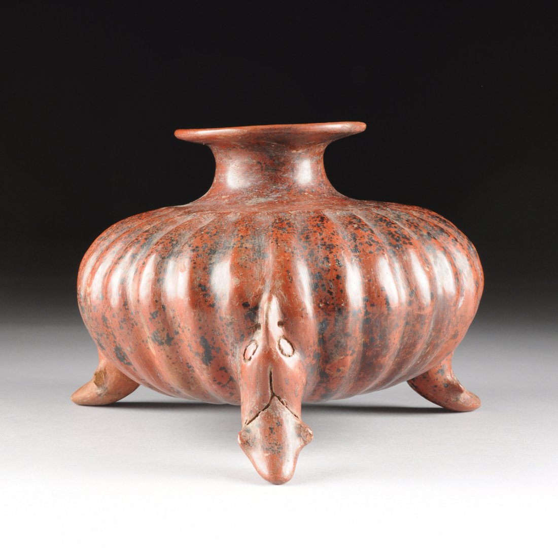 A PRE-COLUMBIAN BLACK SPECKLED RED PAINTED GOURD FORM: A PRE-COLUMBIAN BLACK SPECKLED RED PAINTED GOURD FORM EARTHENWARE VASE, COLIMA, WEST COAST, MEXICO, POSSIBLY 300 A.D. - 950 A.D., of compressed circular tripod form with sides modeled as continuous ve