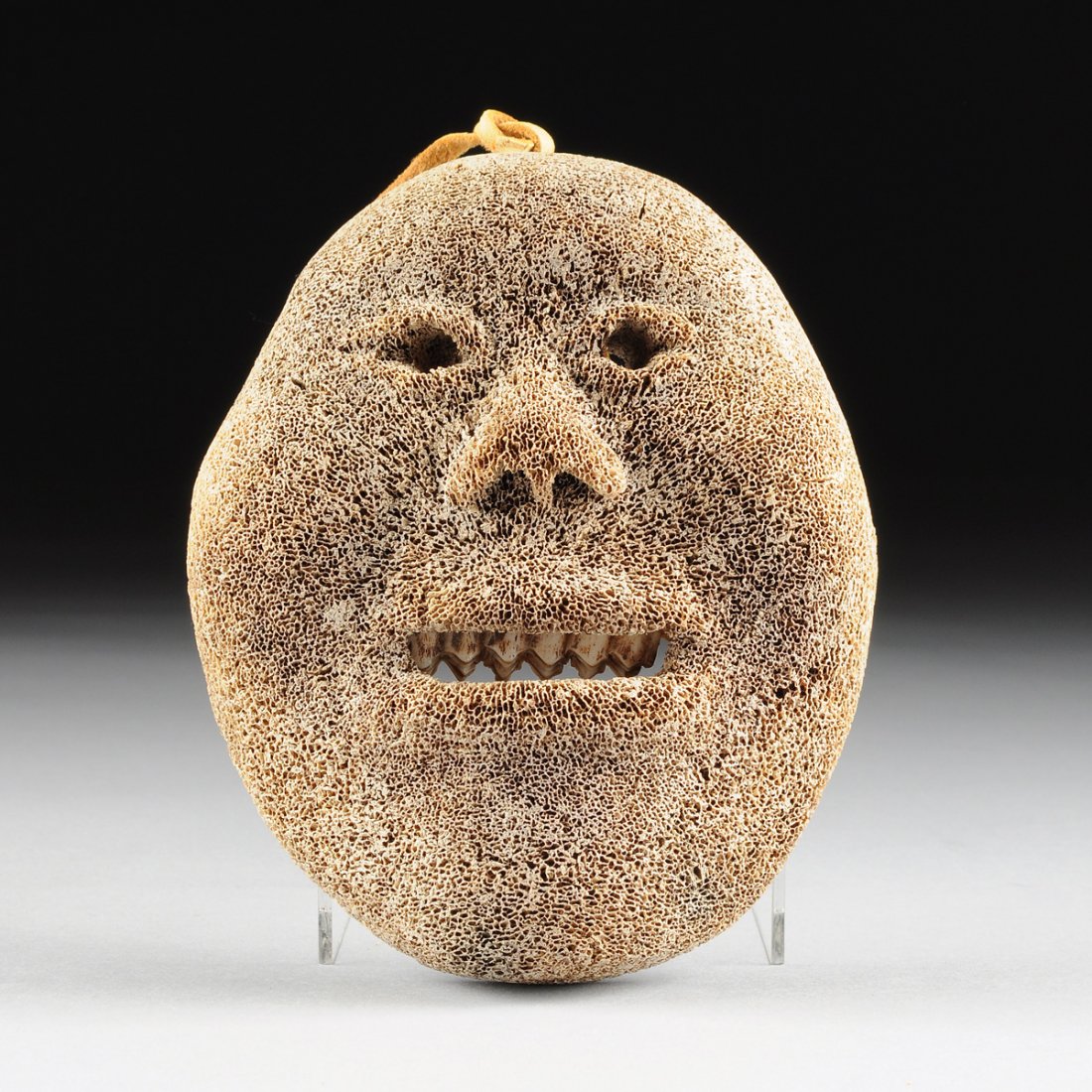 AN ESKIMO INUIT CARVED WHALE BONE MASK, 20TH CENTURY,: AN ESKIMO INUIT CARVED WHALE BONE MASK, 20TH CENTURY, the shaped oval form human face with a naturalistically detailed smiling expression, enclosing reticulated eyes within conforming eyelids above a 