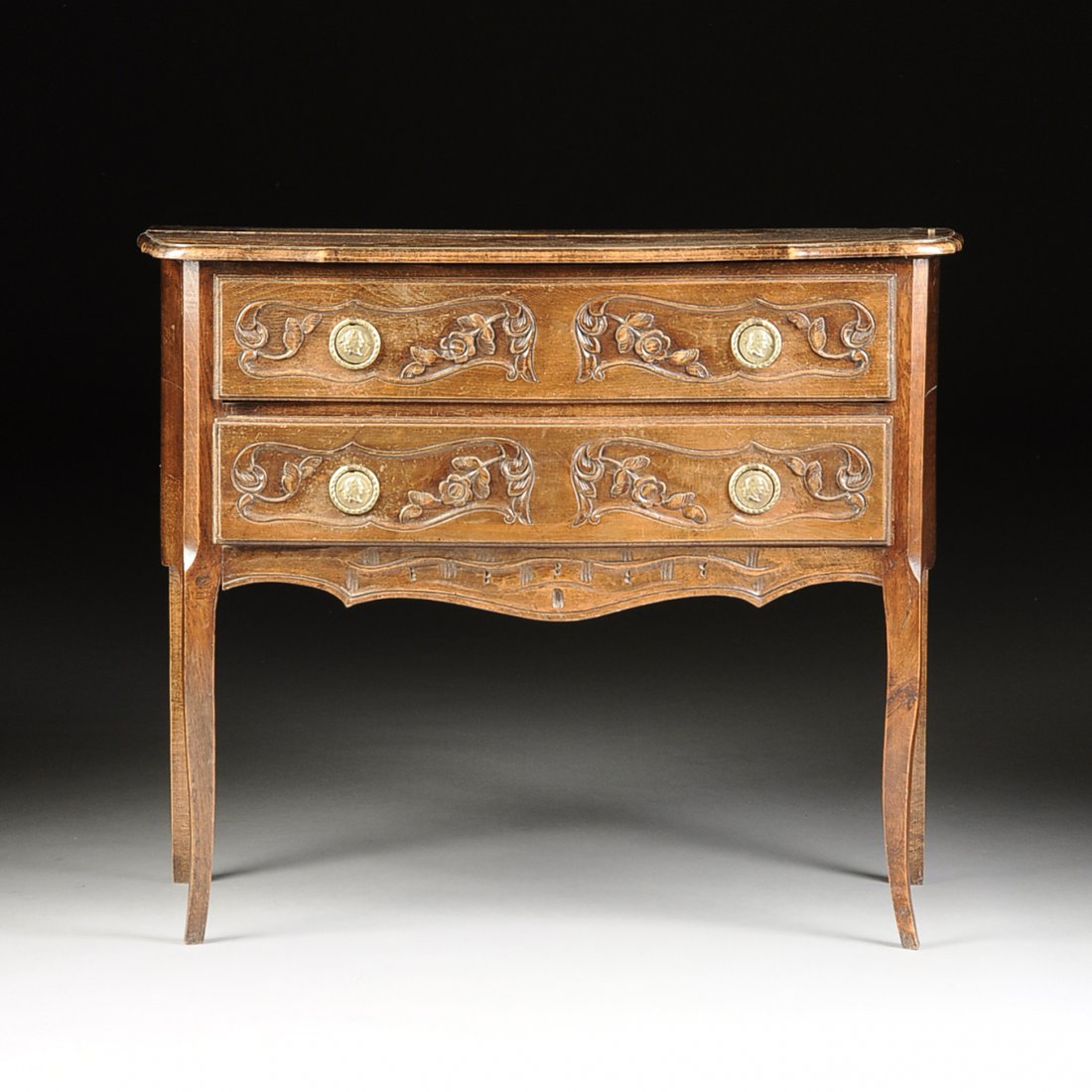 A FRENCH PROVINCIAL CARVED CHESTNUT TWO DRAWER COMMODE,: A FRENCH PROVINCIAL CARVED CHESTNUT TWO DRAWER COMMODE, 20TH CENTURY, the serpentine rectangular top, above two drawers enclosing scrolling recessed panels with blossoming foliage carvings in relief a