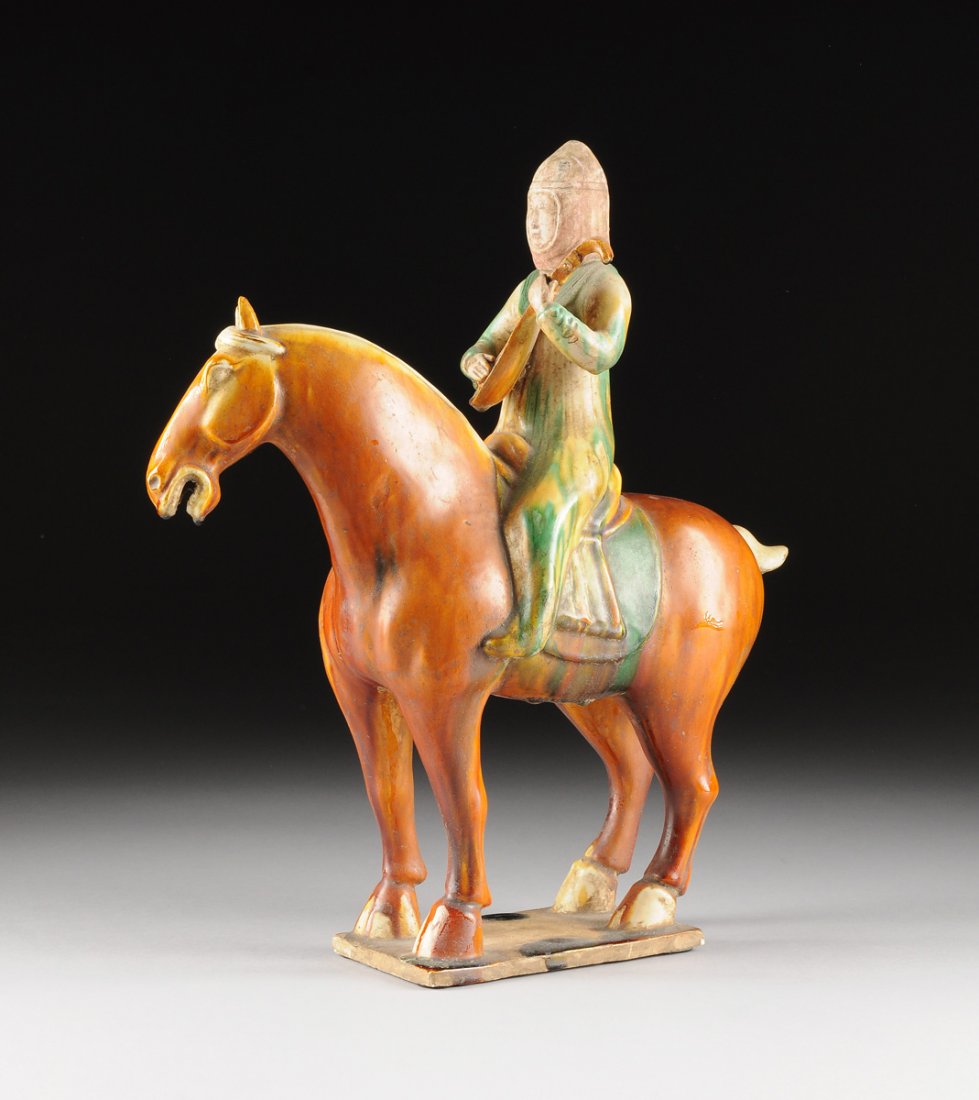A CHINESE SANCAI GLAZED EQUESTRIAN MAIDEN MUSICIAN,: A CHINESE SANCAI GLAZED EQUESTRIAN MAIDEN MUSICIAN, in the Tang Dynasty style, modeled as a cut mane horse standing four square on a rectangular base, supporting a long robed maiden with an unglazed c