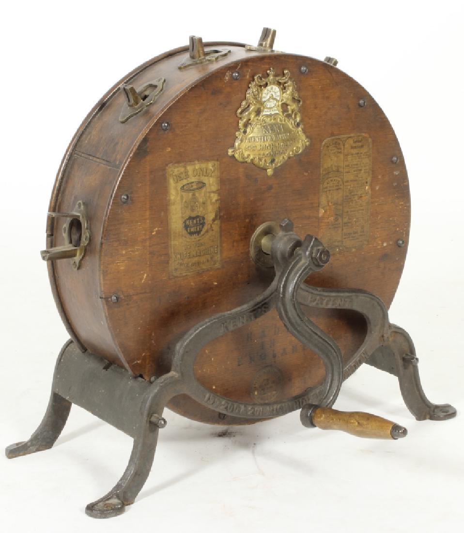 English Circular Mechanical Knife Cleaner c. 1900: A Kent's knife cleaner, with circular oak case with brass fittings mounted on cast-iron legs, the case bearing a brass maker's plate inscribed "Kent / Patentee & Manufacturer / 199 High Holborn / Lond