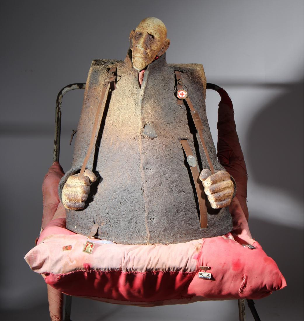 Czeslaw Podlesny, Mixed Media Figurative Sculpture: (Polish, b.1959). Titled "The Hiker". Mixed media, cast figure, metal strapping. Cast figure placed on metal two wheel cart/dolly with fabric cushion and fabric wrapped parts, political lapel pins att