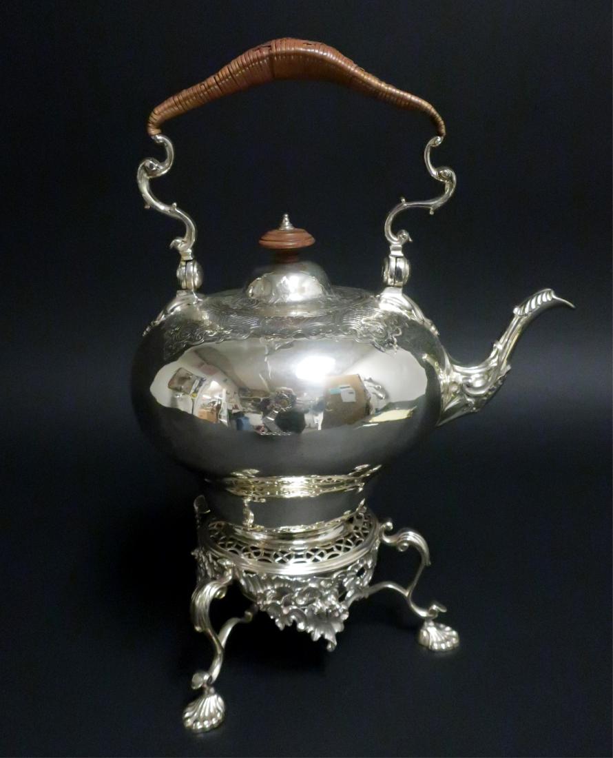 George III Silver Tea Kettle on Stand, London 1755: Engraved with diaperwork at the shoulder and with a crest, leaf-capped handle terminals and spout, raffia-wrapped handle, the stand with pierce shellwork decoration on three leaf-capped scroll legs en