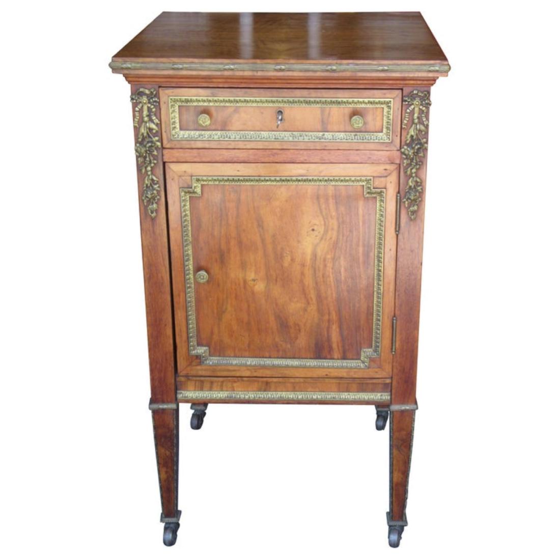 Louis XVI Style Ormolu Bedside Cabinet 19th c.: A wood and ormolu bedside cabinet with one drawer and one large storage area behind a finely grained wood door, tapered legs terminate on casters. H 33 in. x W 18.5 in. x D 18.5 in. (MTKI8204)(TC)