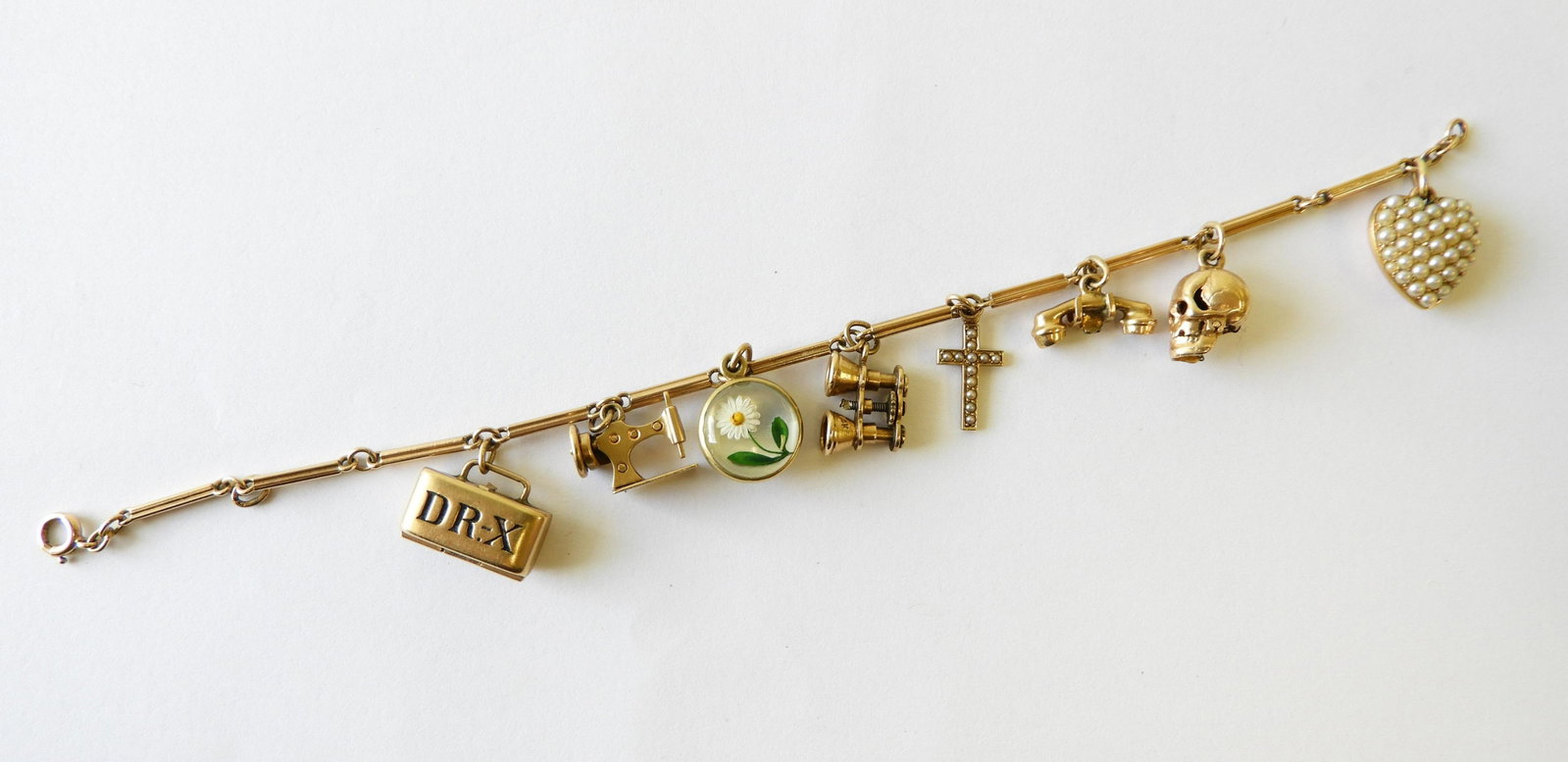 14K Charm Bracelet: 8 charms including Dr. X brief case with bloody hatchet and saws inside, sewing machine, binoculars, telephone, cross with pearls, heart with pearls, skull, and one with butterfly & daisy. Gross weigh