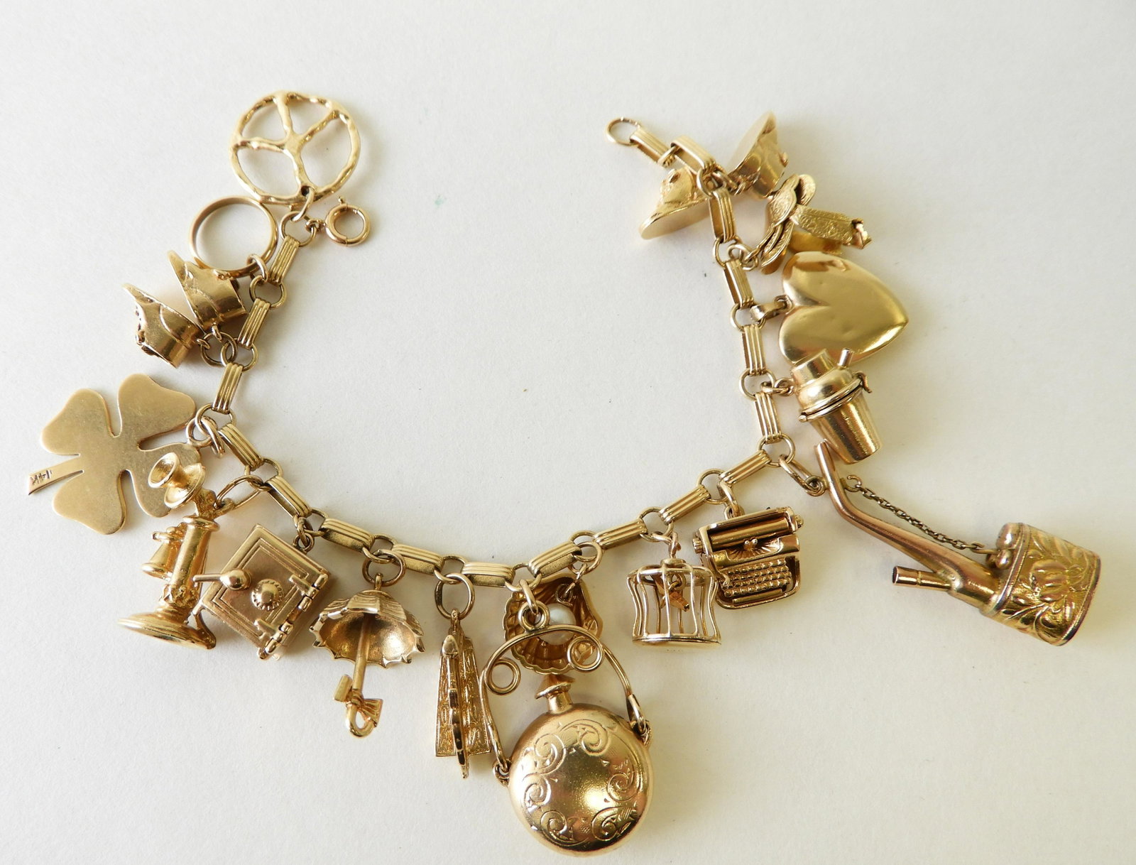 14K Yellow Gold Charm Bracelet: Charms include peace sign, baby shoe, umbrella, cello, type writer, heart, saddle, telephone, clam shell, bird cage, shaker, four leaf clover, etc. Safe has folded up $1 bill inside. 7" long. Gross we