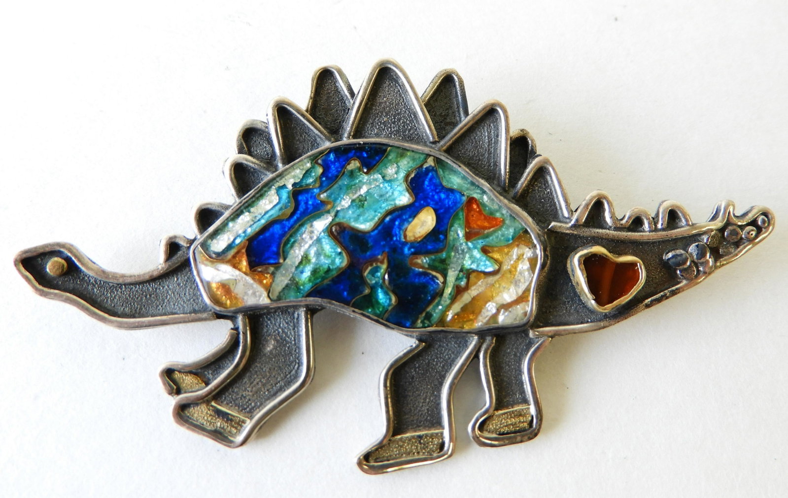 Sterling, 14k, 22k Dinosaur Brooch: Stegosaurus comprised of sterling silver, 14k gold, and 22k gold with Cloisonne enamel body in blue, aqua, yellow and white. Signed Kristin Holeman on back. 3" wide. Property from the estate of Rosali