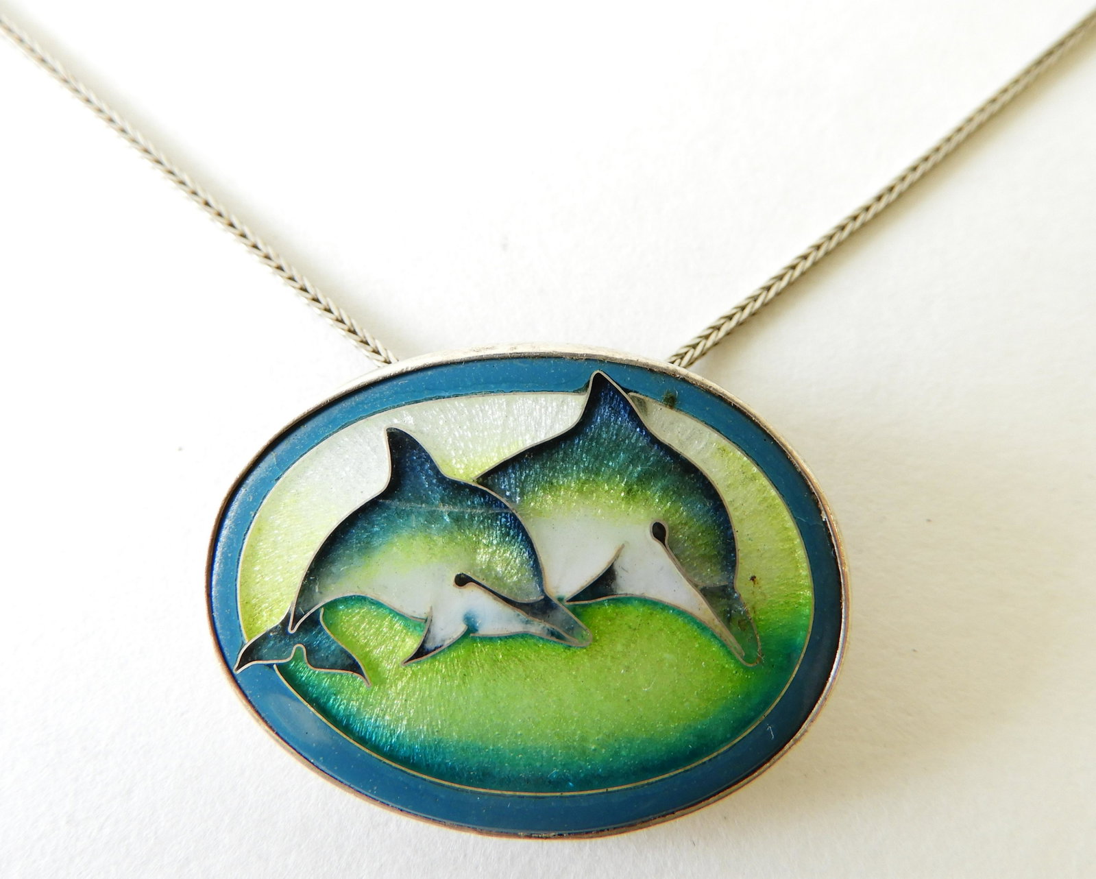 Dolphin Pendant by Falker, 1989: Two cloisonne enamel dolphins set in sterling silver. Back signed 'Falker 1989 Sterling' o an 18" sterling silver chain. 1.25" wide Property from the estate of Rosalie Coe Weir
