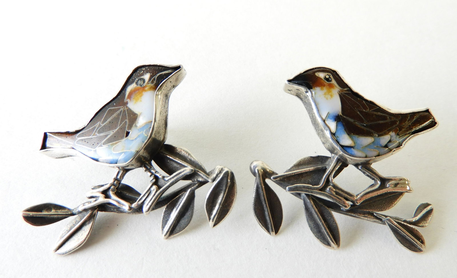 Pair of Enamel Sparrow Earrings: Pair of sterling silver earrings with cloisonne enamel sparrows perched on branches. Marked & initial KH (Kristin Holeman) on back. 1" x 1.5" Property from the estate of Rosalie Coe Weir