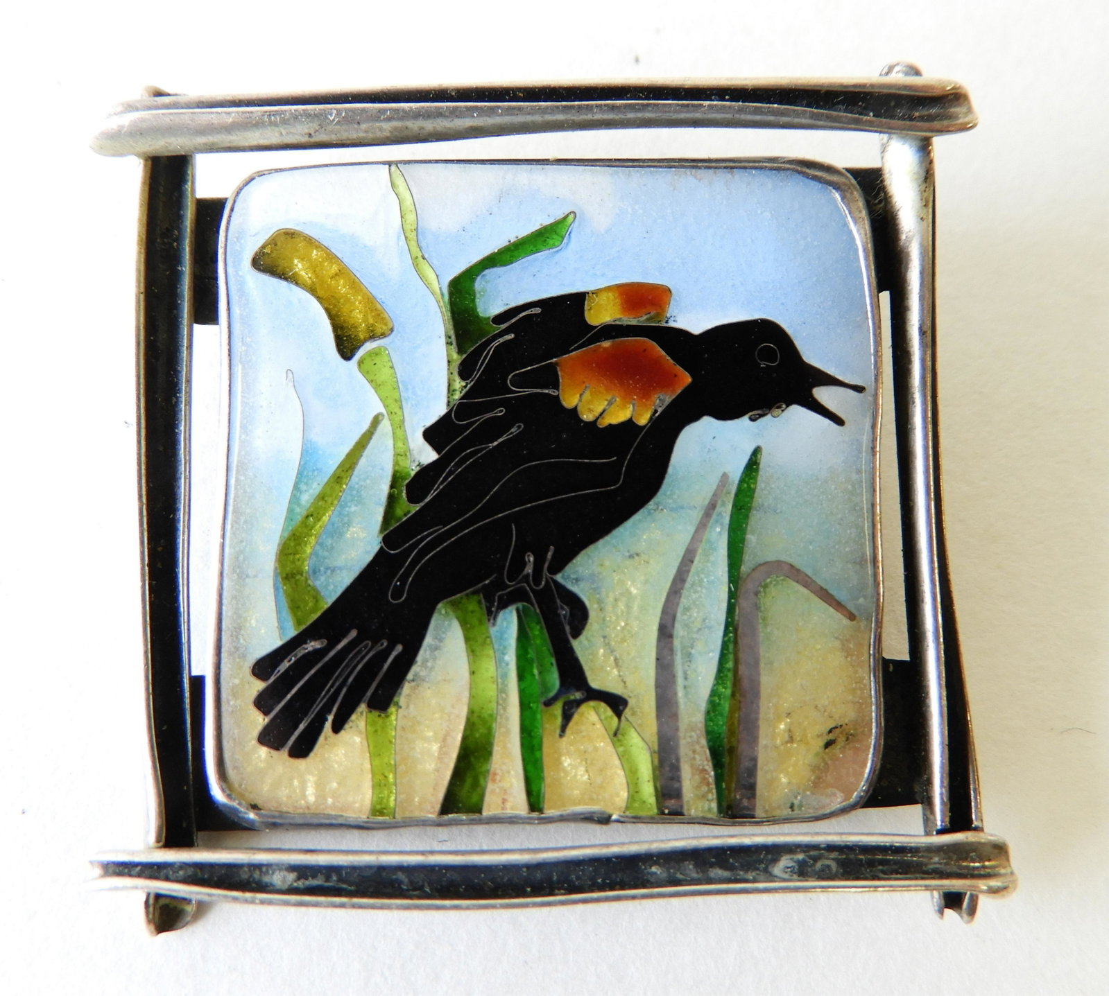 Red-Winged Blackbird Enamel Brooch: Sterling Silver brooch with cloisonne enamel red-winged black bird perched on a cat tail. 1.5" square. Unsigned but most likely Kristin Holeman. Property from the estate of Rosalie Coe Weir