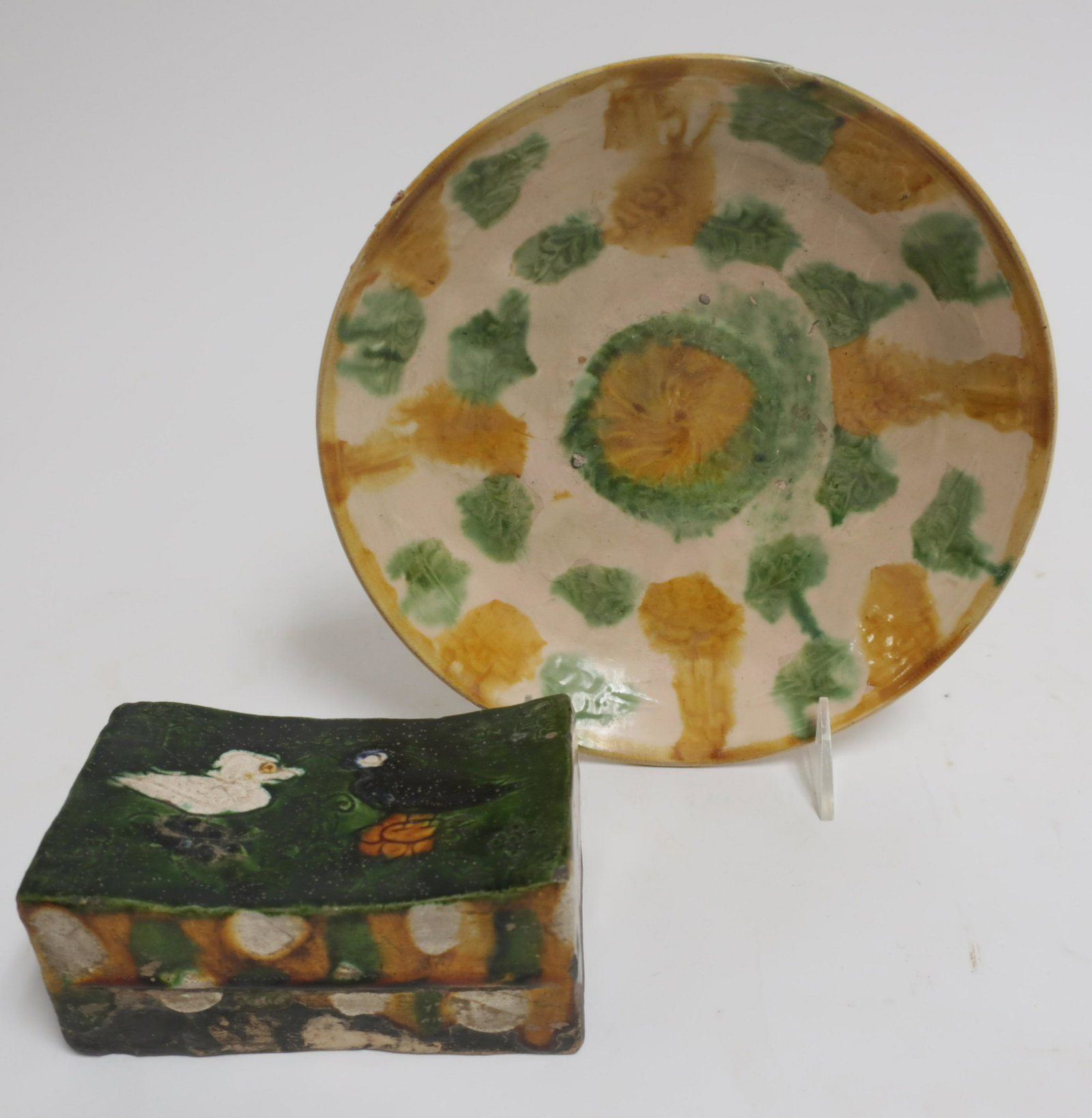 Sancai Glazed Dish and Pillow: Footed dish with a light molded design and a spotted sancai glaze, likely Liao Dynasty (907-1125 CE). Offered with a small earthenware pillow in a sancai glaze over incised design. Likely Tang ,c. 8th