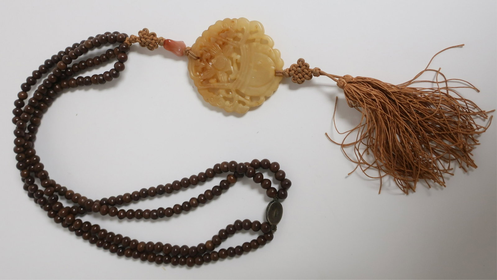 Carved Jade Tassel Pendant: Suspended from two strands of wooden beads, sterling silver clasp. Dimensions: Jade is 2.25 x 2.25" (LCA304)(EL)