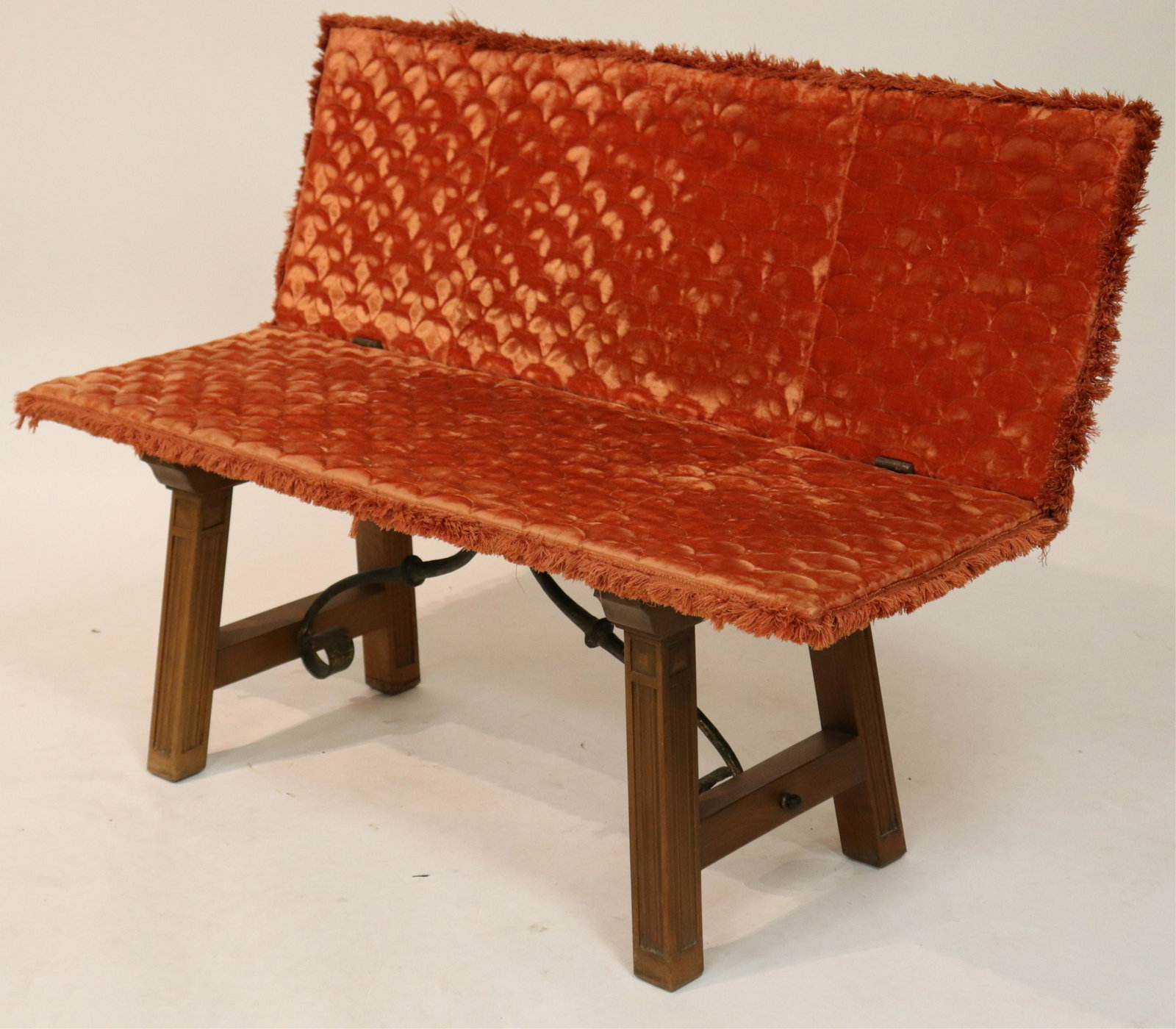 Spanish Style Fold-Over Bench: S-form iron stretchers with threaded tensioners; iron hinges; raked and panel carved legs; upholstered in fringed muted orange velvet.; wood in a matte natural finish. Traces of gilt paint on iron. Fo