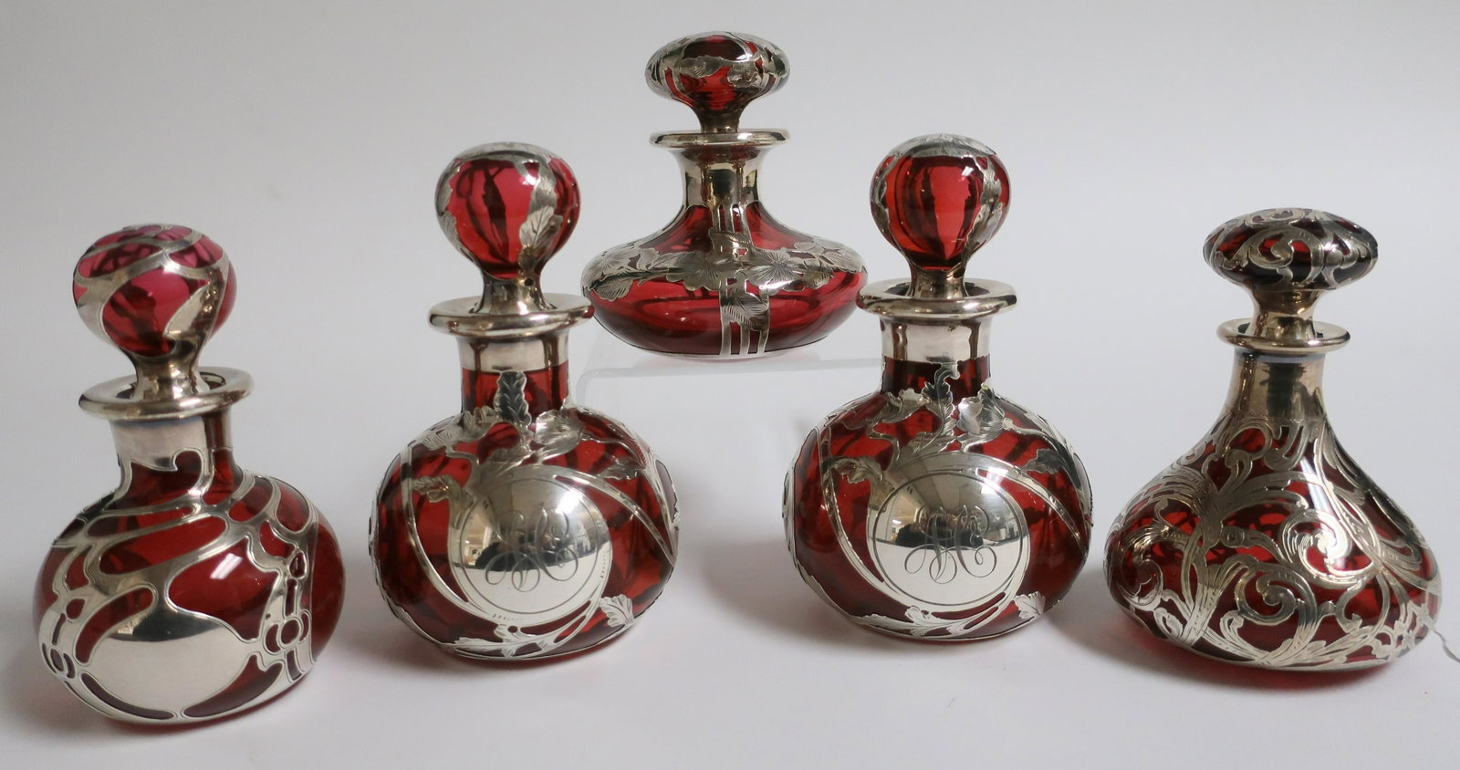 5 Sterling Silver Overlay Ruby Red Perfumes: 5 Sterling Silver Overlay Ruby Red Perfumes; includes a pair by Gorham D941, 5 1/2" H x 3" dia., monogrammed, ground small chip to one stopper and and/or slightly cloudy bottom. Alvin squash form R313