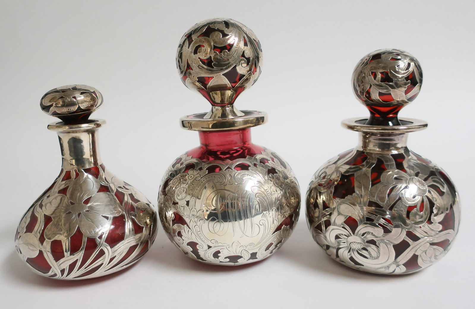 3 Sterling Silver Overlay Ruby Red Perfumes: 3 Sterling Silver Overlay Ruby Red Perfumes; Gorham S682 licensed, monogram, 7 1/4" H x 4 1/4" dia, cloudy ring to bottom; sterling silver deposit 45 M. Scooler 6 1/2" H x 4" dia., chipped stopper end