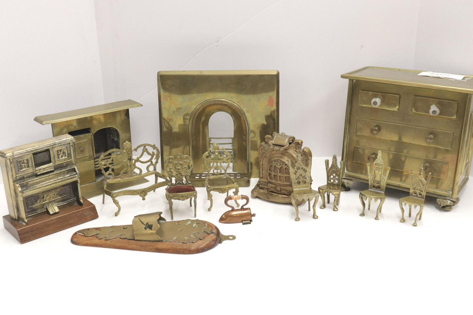 Collection Antique Brass Dollhouse Furnishings: Includes: Sadiron tape measure with agate handle C1880. (3) coal burning style hearths/fireplaces. Chest of drawers. Player piano. (6) side chairs. Bench. Wall mount holder. Fender. Dimensions: Sadiro