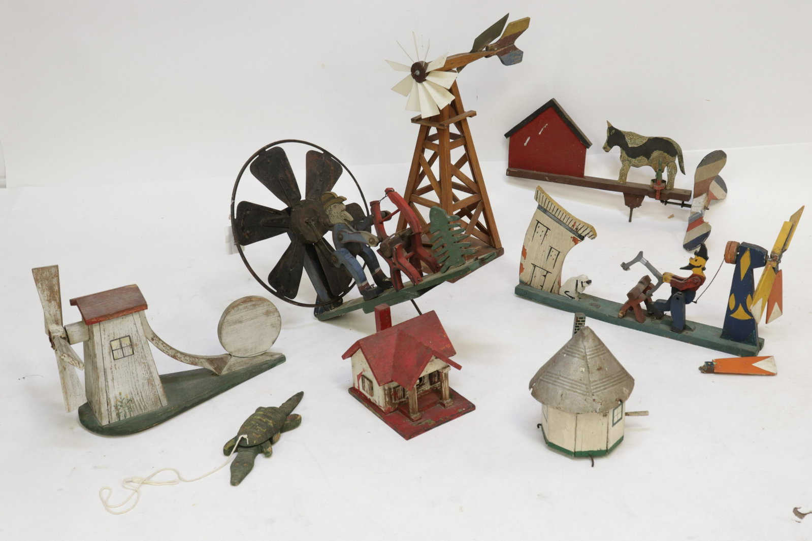Vintage Folk Art - Whirligigs, Birdhouses, Toy: Cut and shaped painted wood, metal. Whirligigs: one with cooling fan wind catcher; water pump tower; (2) with sawbucks; milking cow. (2) birdhouses, one with tin can roof. Alligator pull-toy. Dimensio