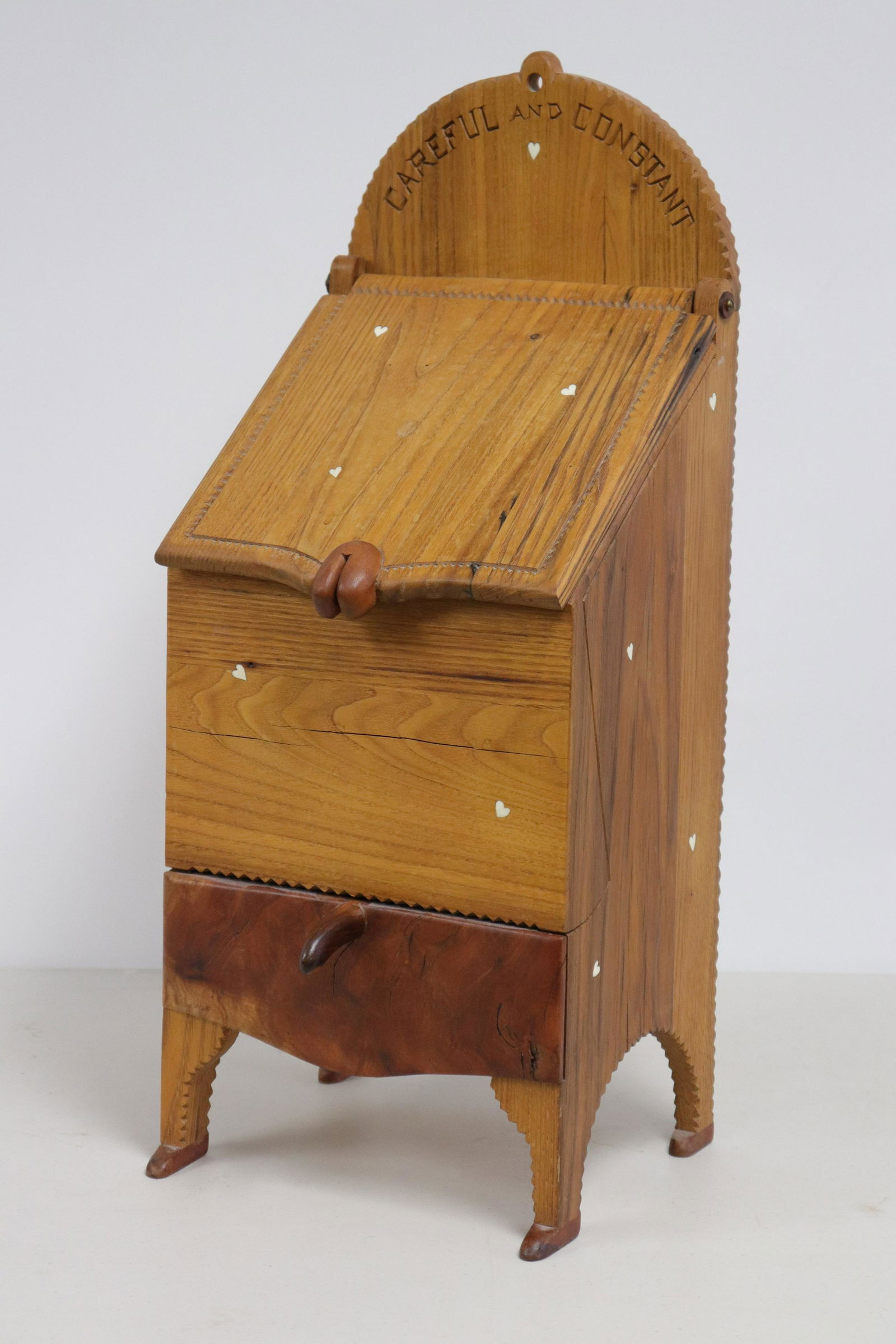 Tommy Simpson "Careful And Constant" Box On Legs: L20C. Mixed woods. Slant top with lift lid. One drawer. Arched base with legs. Shaped lid lift and drawer pull. M.O.P. inlaid hearts, chip notched edges decoration. "Shoe" feet. Vintage doily postcard
