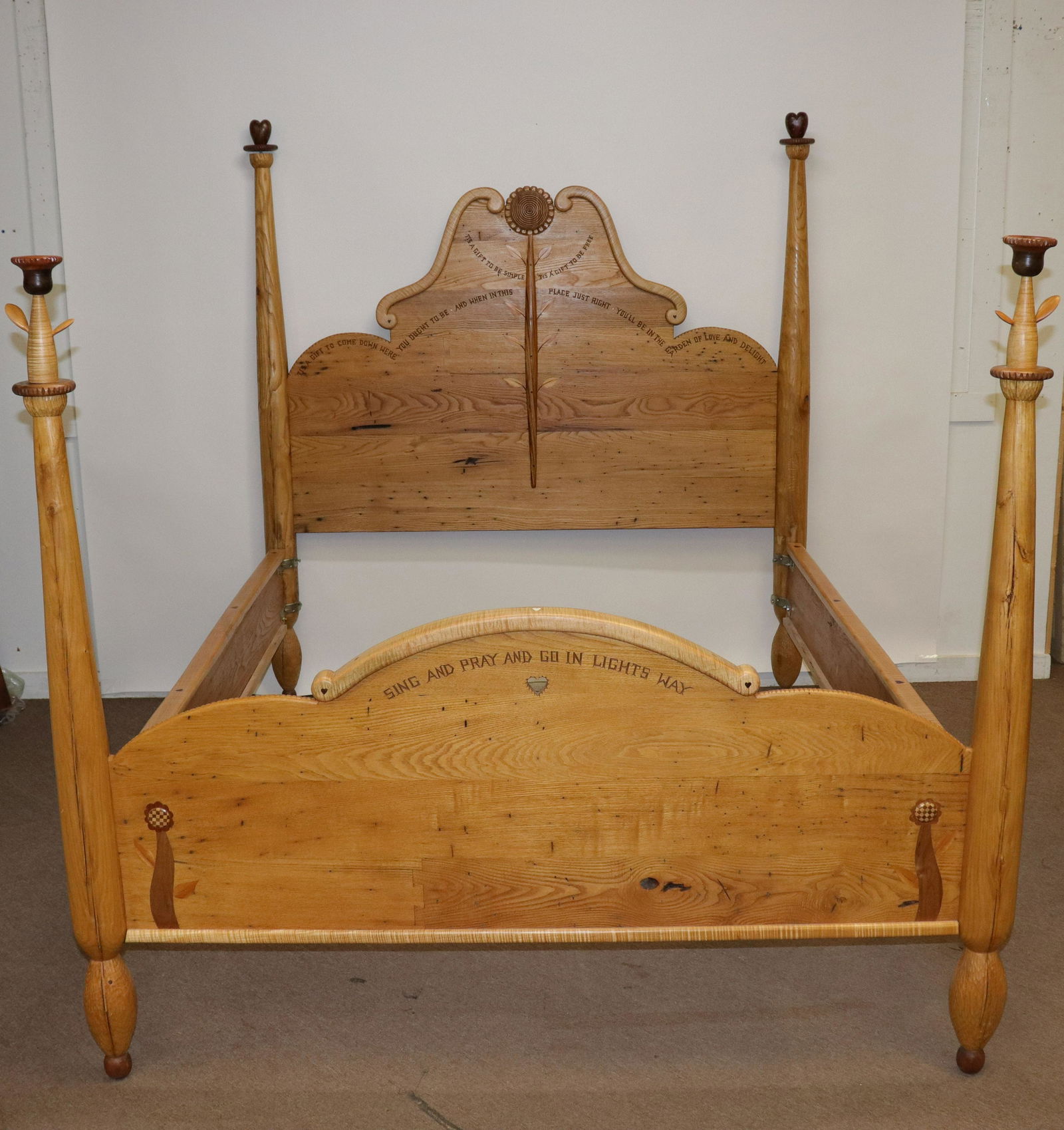 Tommy Simpson "...Simple...Free" Queen Size Bed: L20C. Mixed woods. carve inscribed inscriptions. Punctuations, hearts inlays. Applied spindle stem with carved flowerhead on headboard. Removable post finials. Dimensions: 70.5"H @ top of finial. 78.2